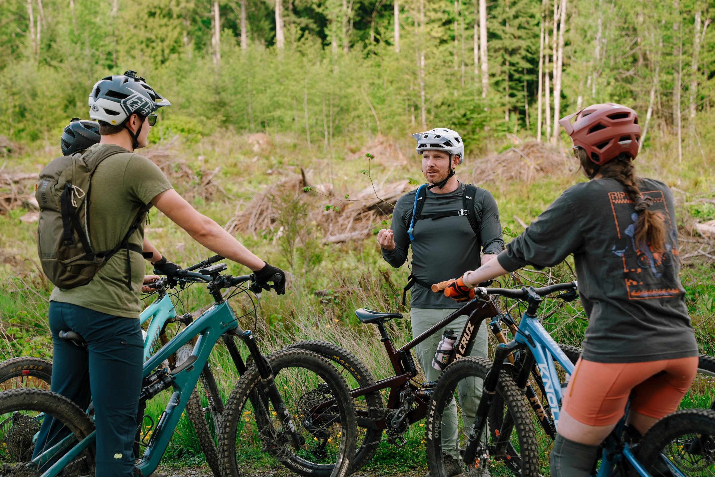 A group of mountain bikers listening to the coach speaking.