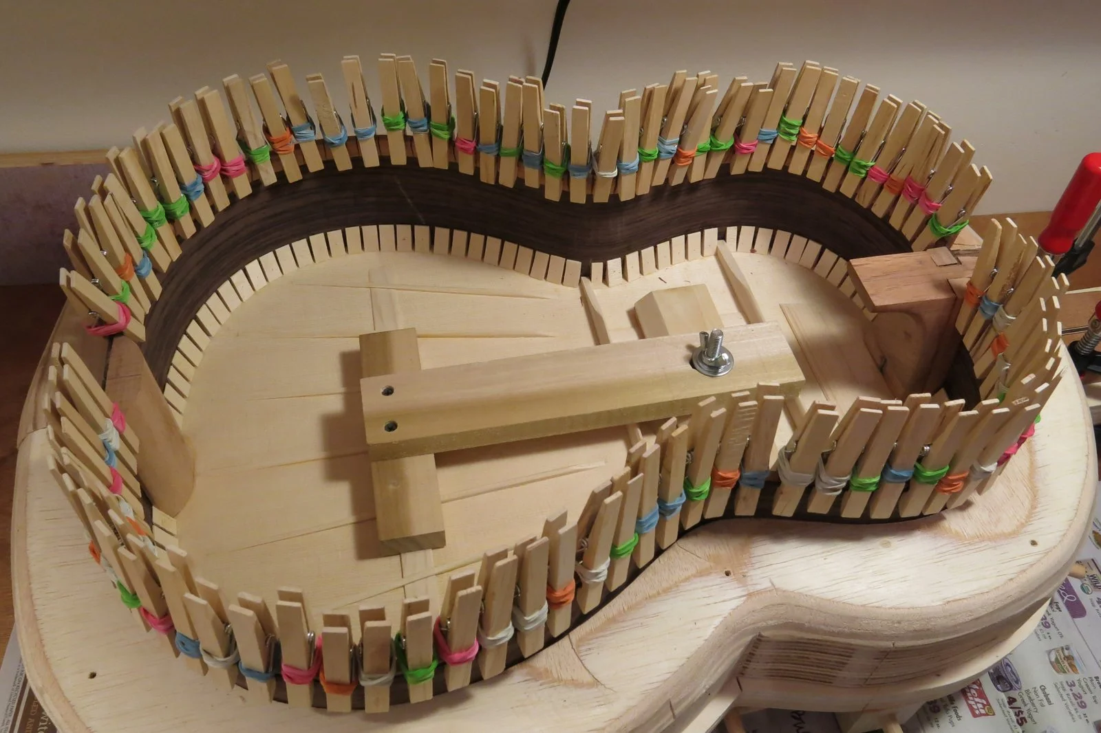 A wooden loom in progress with colorful clips holding the warp threads, mounted on a wooden base.