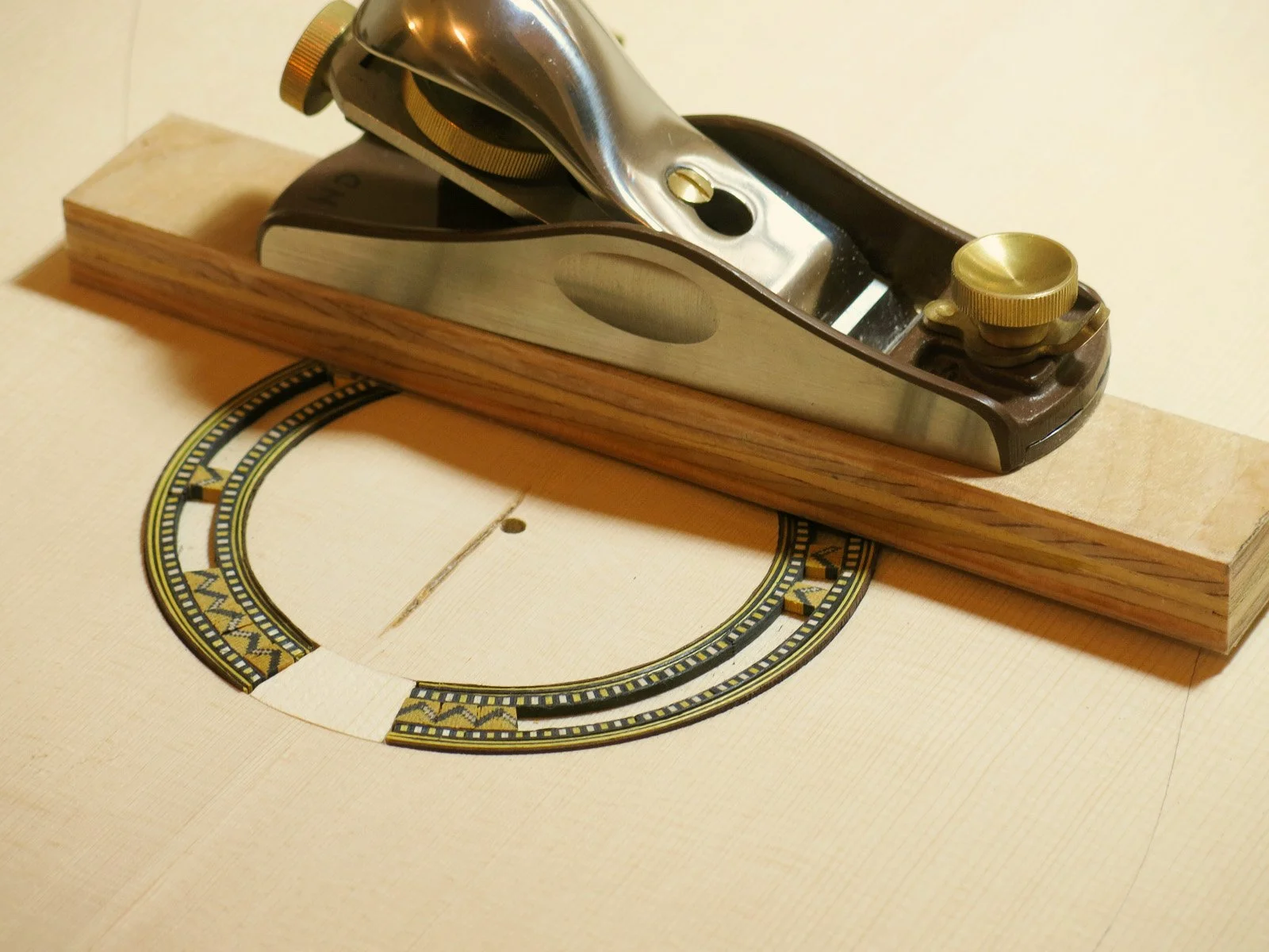 A woodworking plane tool resting on a piece of wood with a decorative semi-circular inlay pattern.