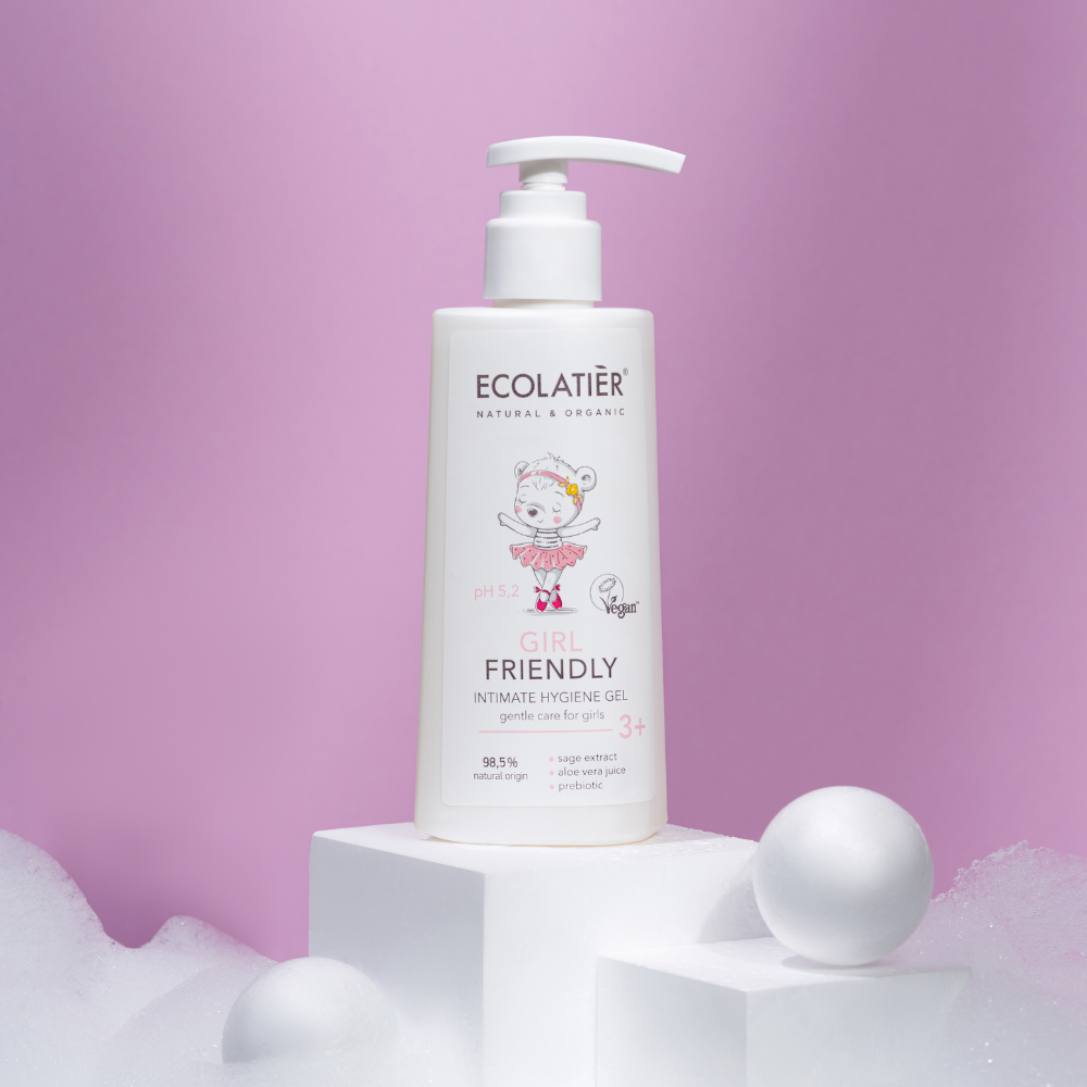 Botella de gel íntimo ecológico para niñas en un fondo rosa y elementos decorativos blancos.
