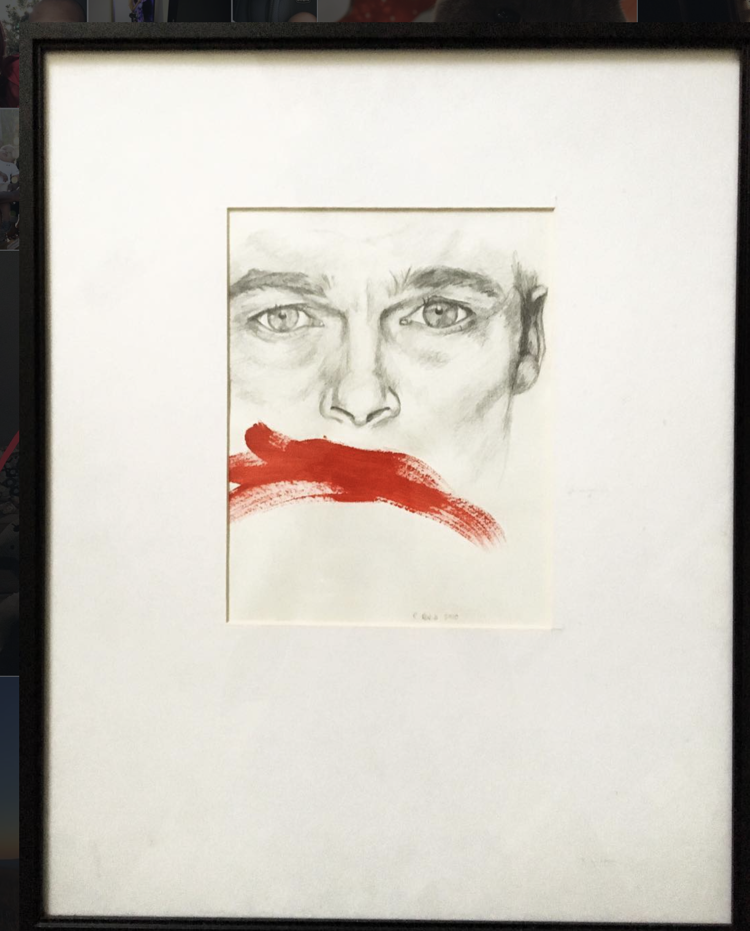 Framed artwork of a pencil sketch of a person's face with red paint across the mouth area.