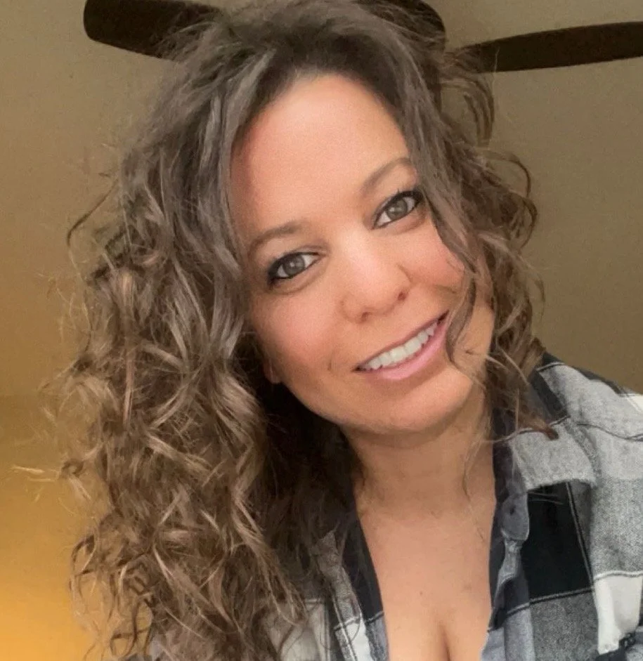 Psychic, medium woman with curly brown hair, smiling, in front of a beige wall.