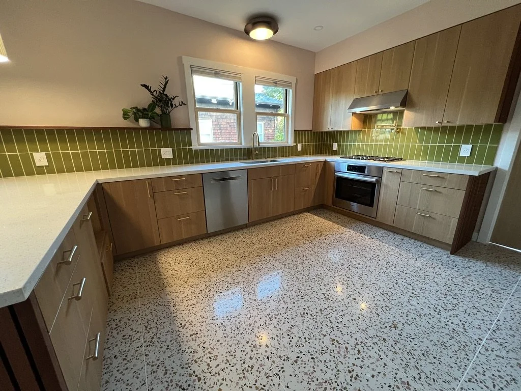 Kitchen with wooden cabinets, green tile backsplash, terrazzo floor, stainless steel appliances, and a window above the sink.