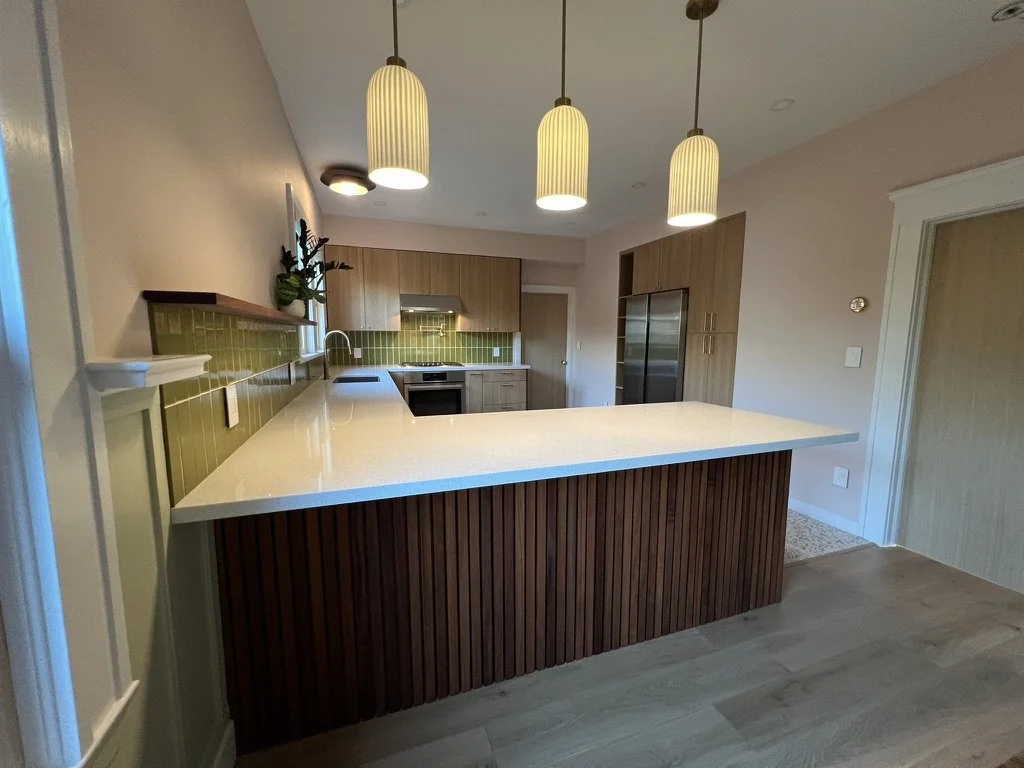 Modern kitchen with a white countertop island, wooden cabinets, green tiled backsplash, and three hanging pendant lights.