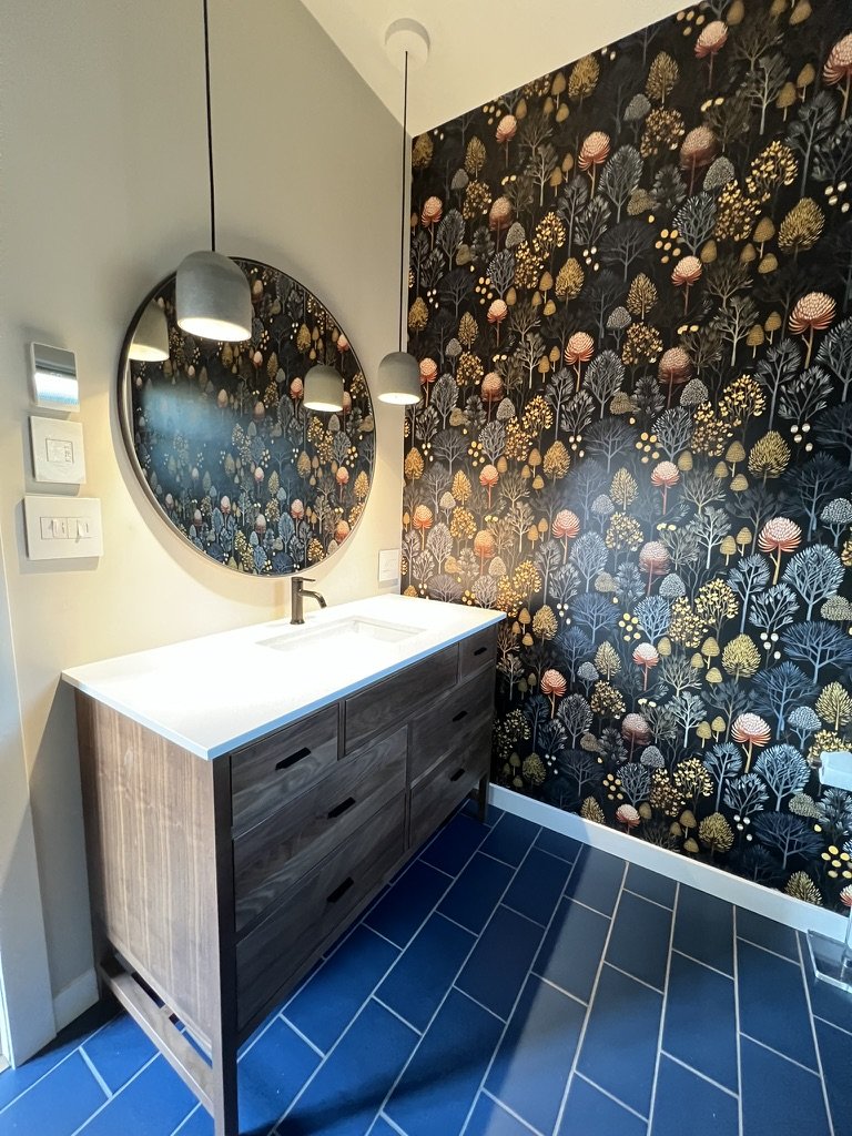 bathroom with patterned wallpaper, wood vanity, and layered material palette