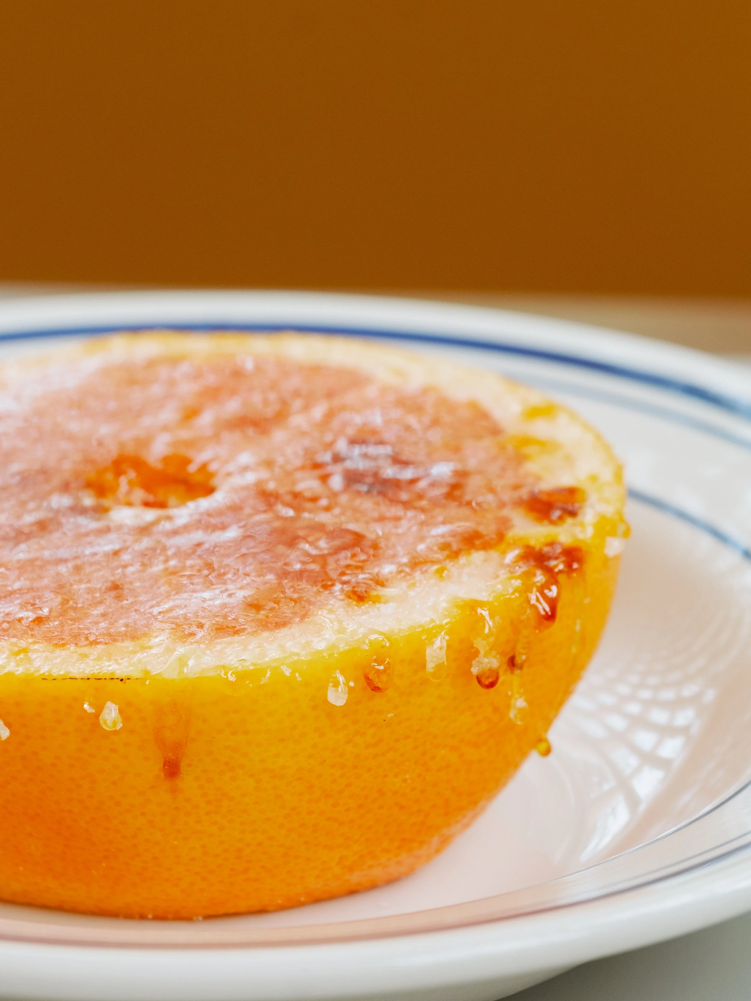 Half grapefruit on a plate with juice dripping down its sides.