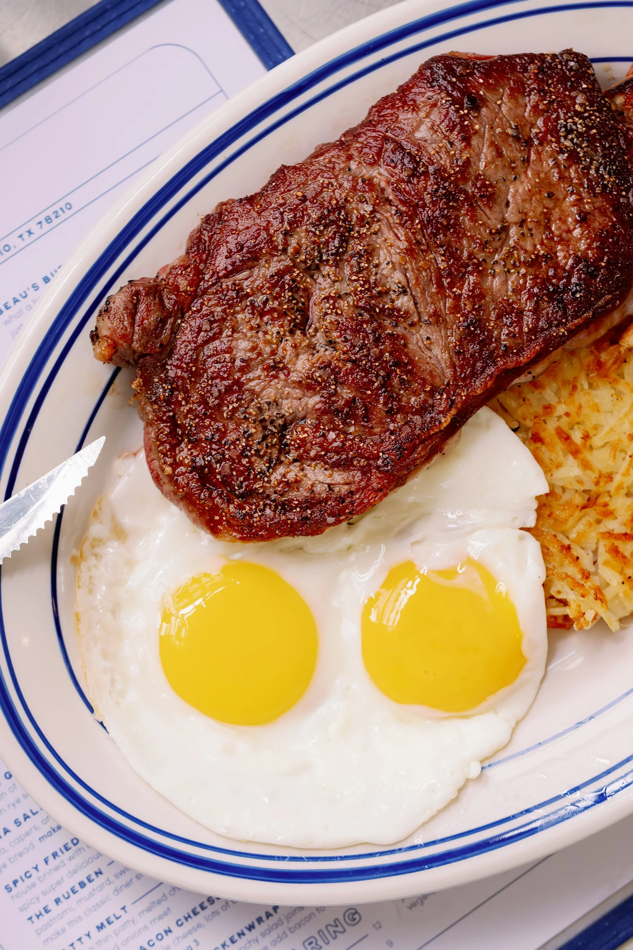 A plate of cooked steak, two fried eggs, hash browns, and toast.