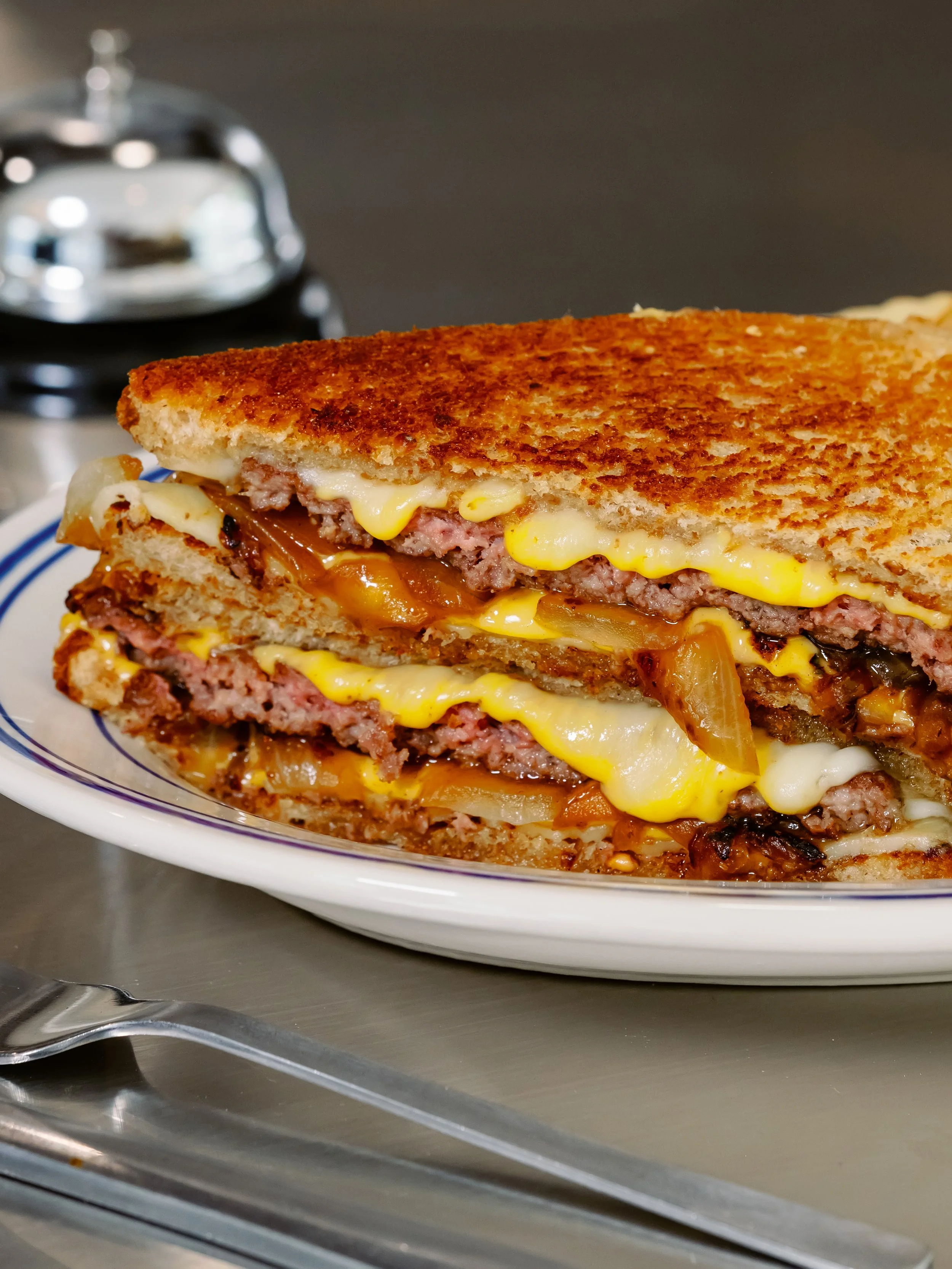 Cross-section of a cheeseburger with sliced beef patties, melted cheese, onions, and condiments on toasted bread.