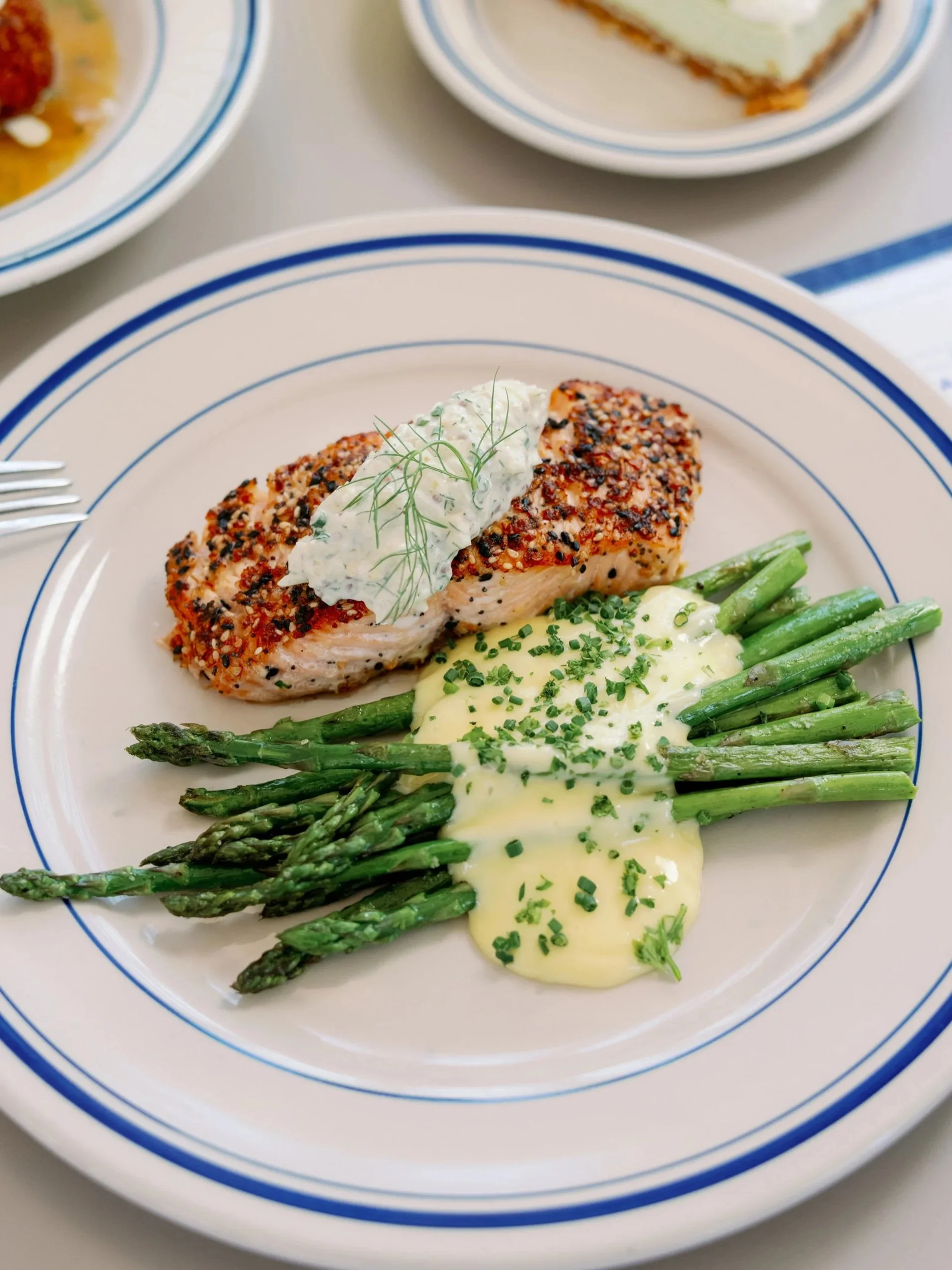 A plate with roasted salmon topped with herb sauce, served with green asparagus spears and creamy mashed potatoes garnished with chopped chives.