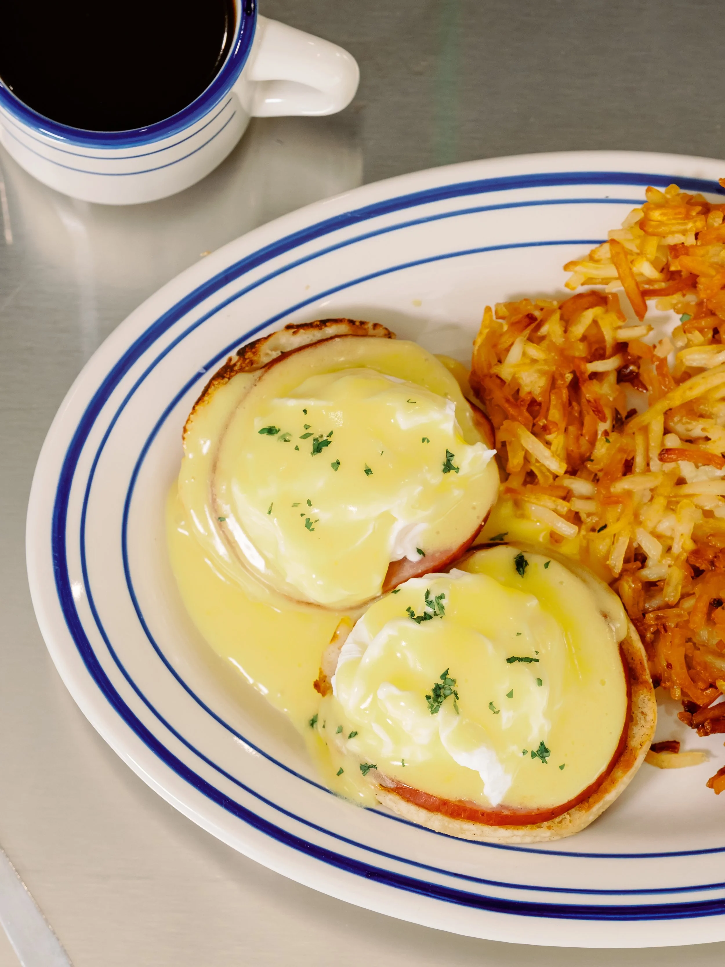 Eggs Benedict with hollandaise sauce, served with hash browns and a side of rice.