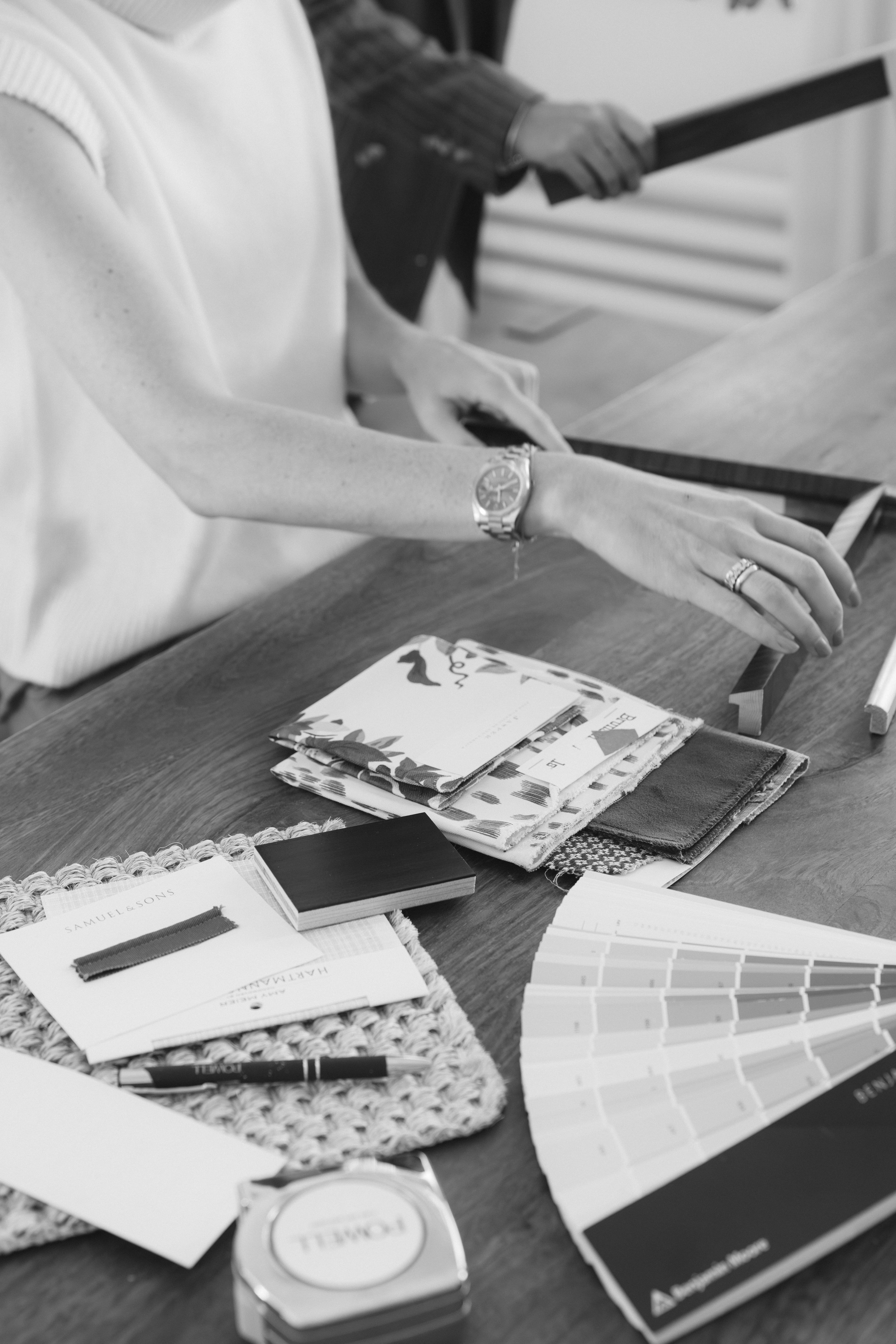 People selecting framing and color samples at a table, with design materials and tools, in an office setting.