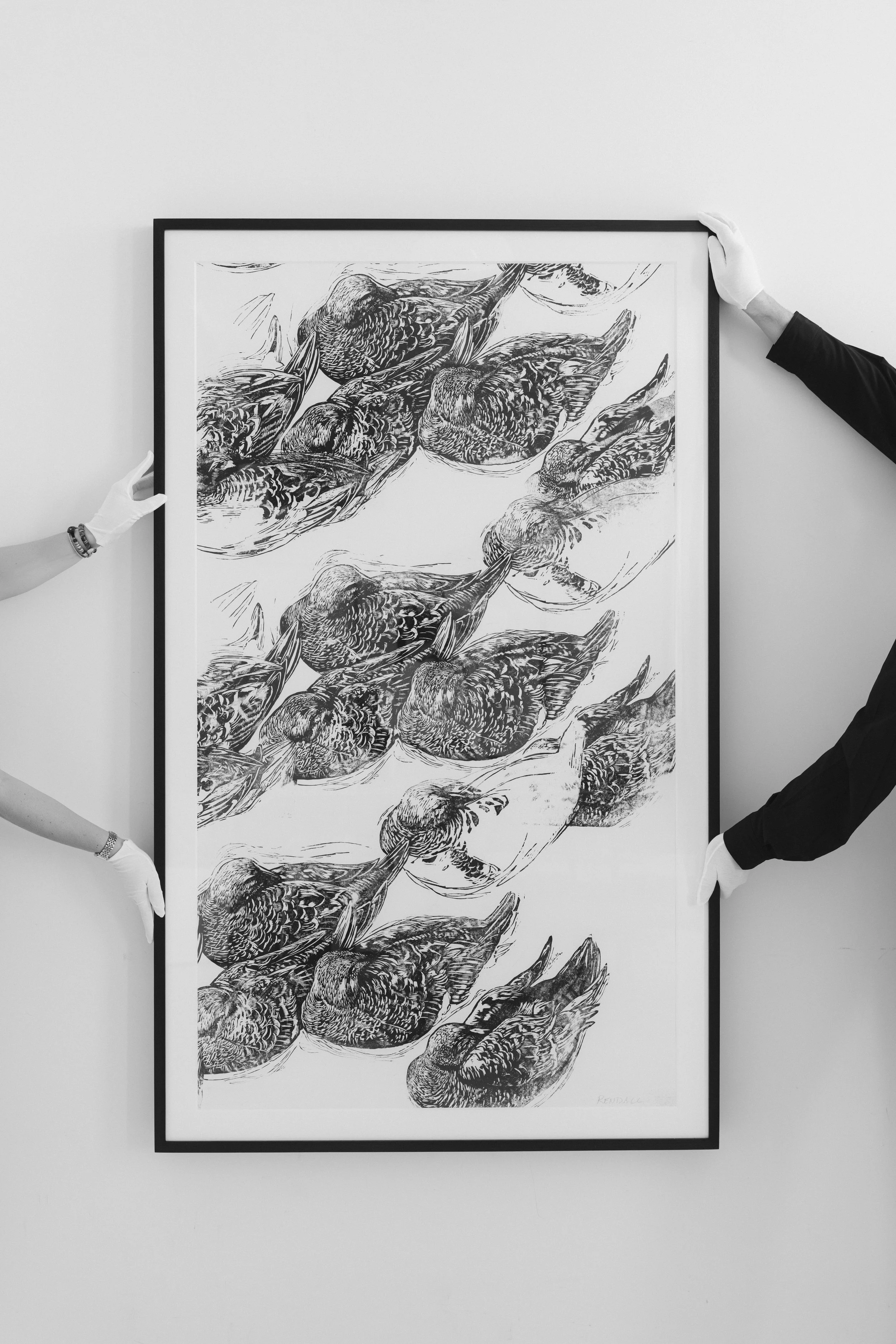 Hands wearing gloves holding a framed black and white artwork depicting a pattern of stylized mallards.