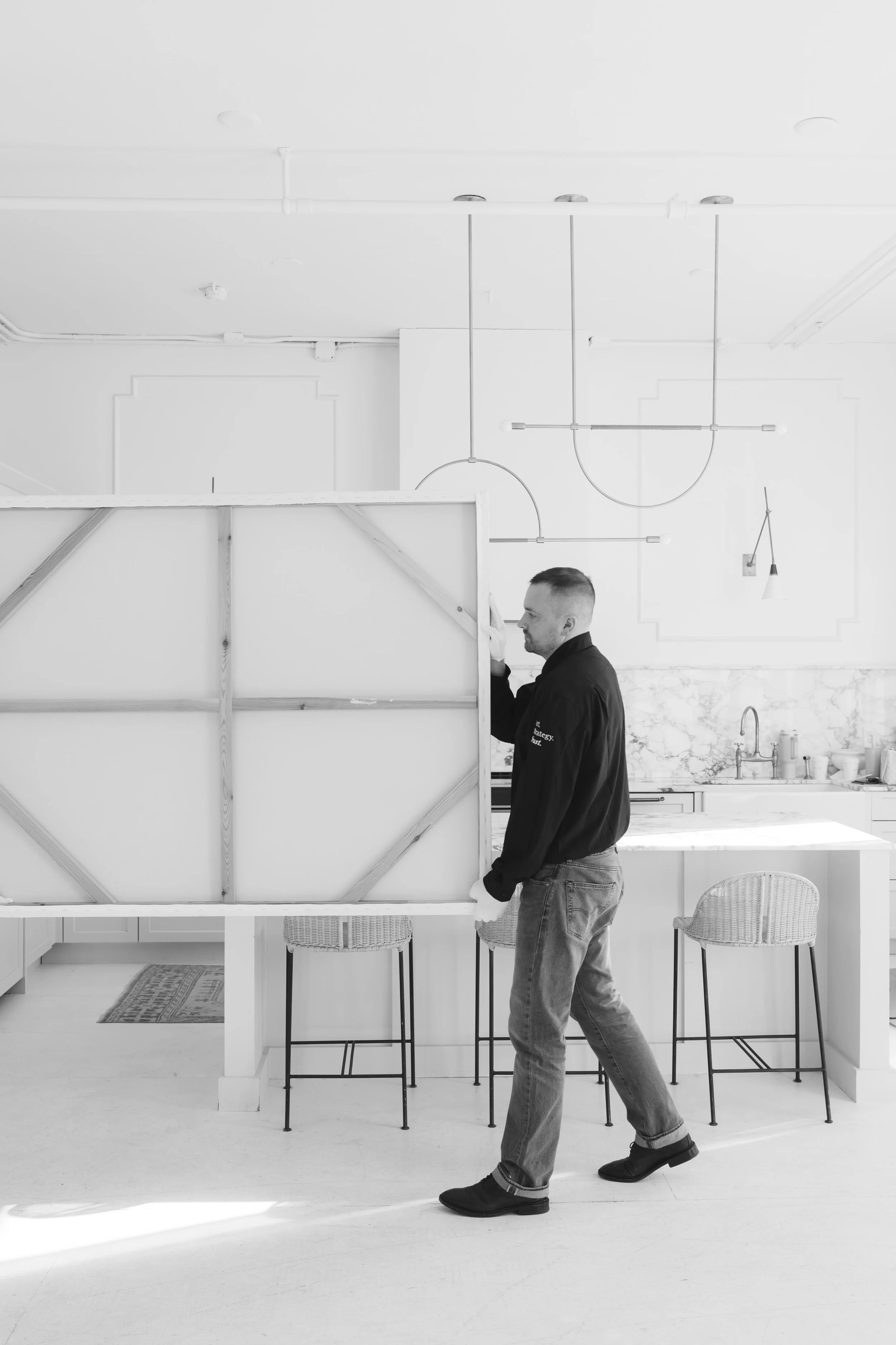 Man standing in a modern kitchen, holding a large canvas, with kitchen island and barstools in the background.
