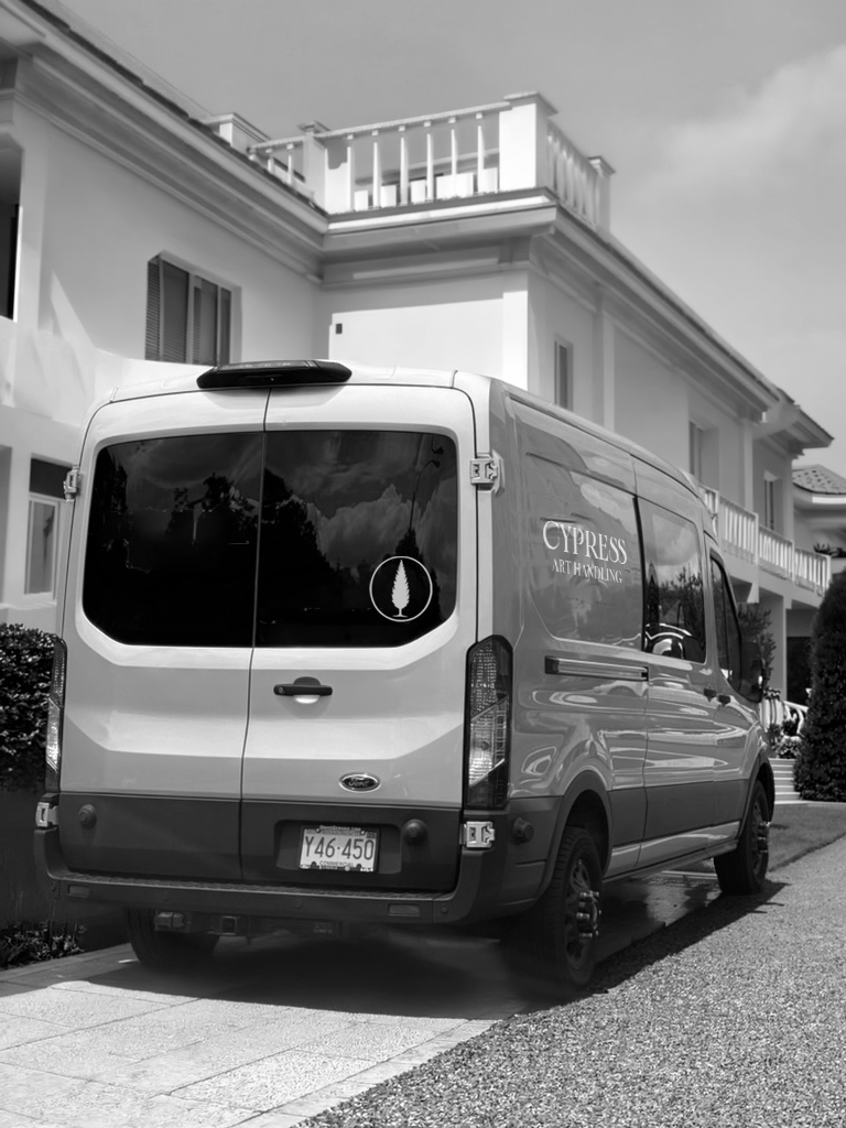 Back view of a business van parked on a residential street in front of a modern multi-story house with balconies.