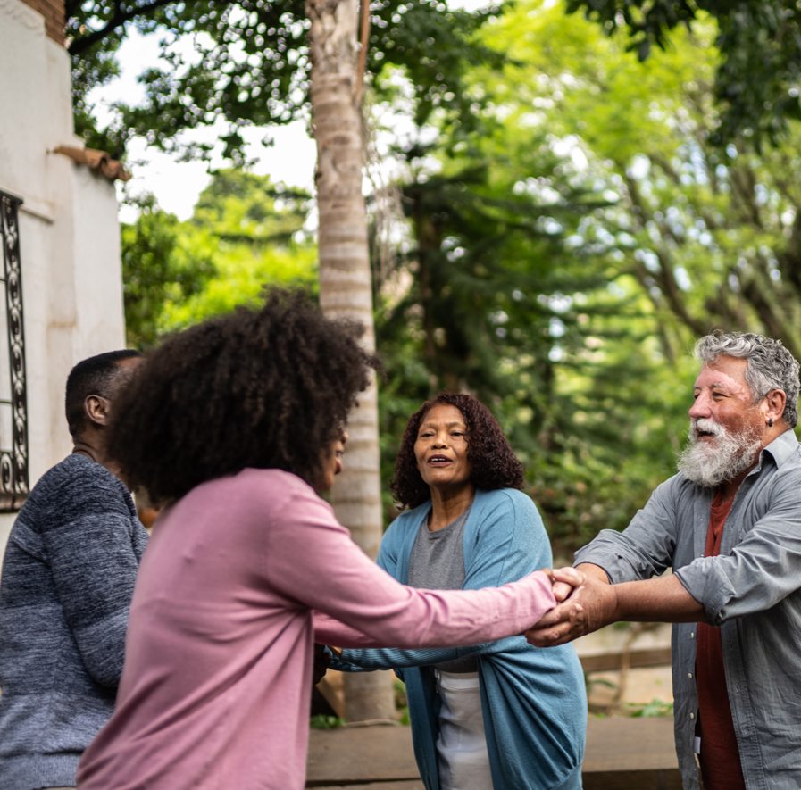 People shaking hands outdoors among trees, with three women and one man, smiling and engaging in friendly interaction.