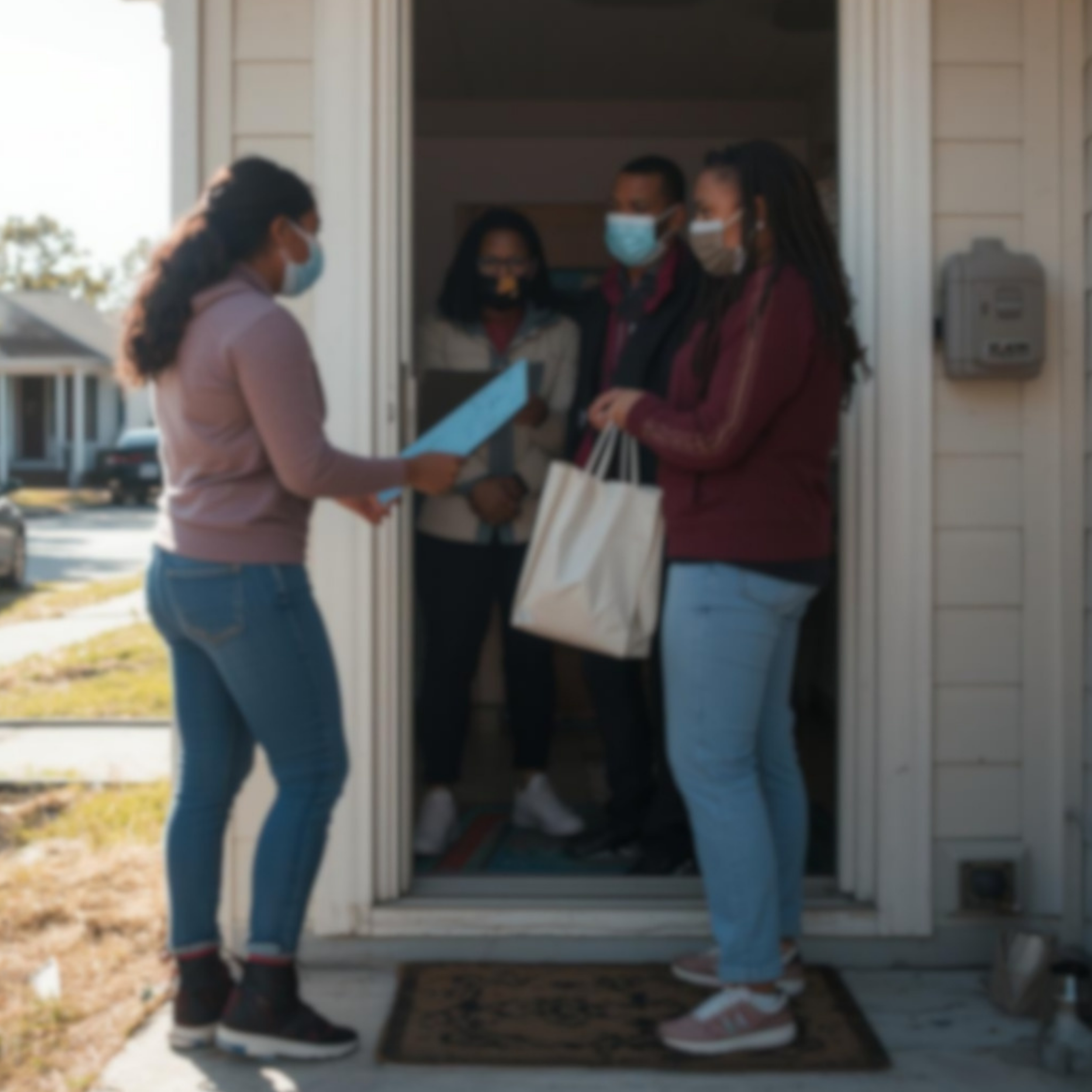 A woman at a door delivering a package to a group of people standing outside.