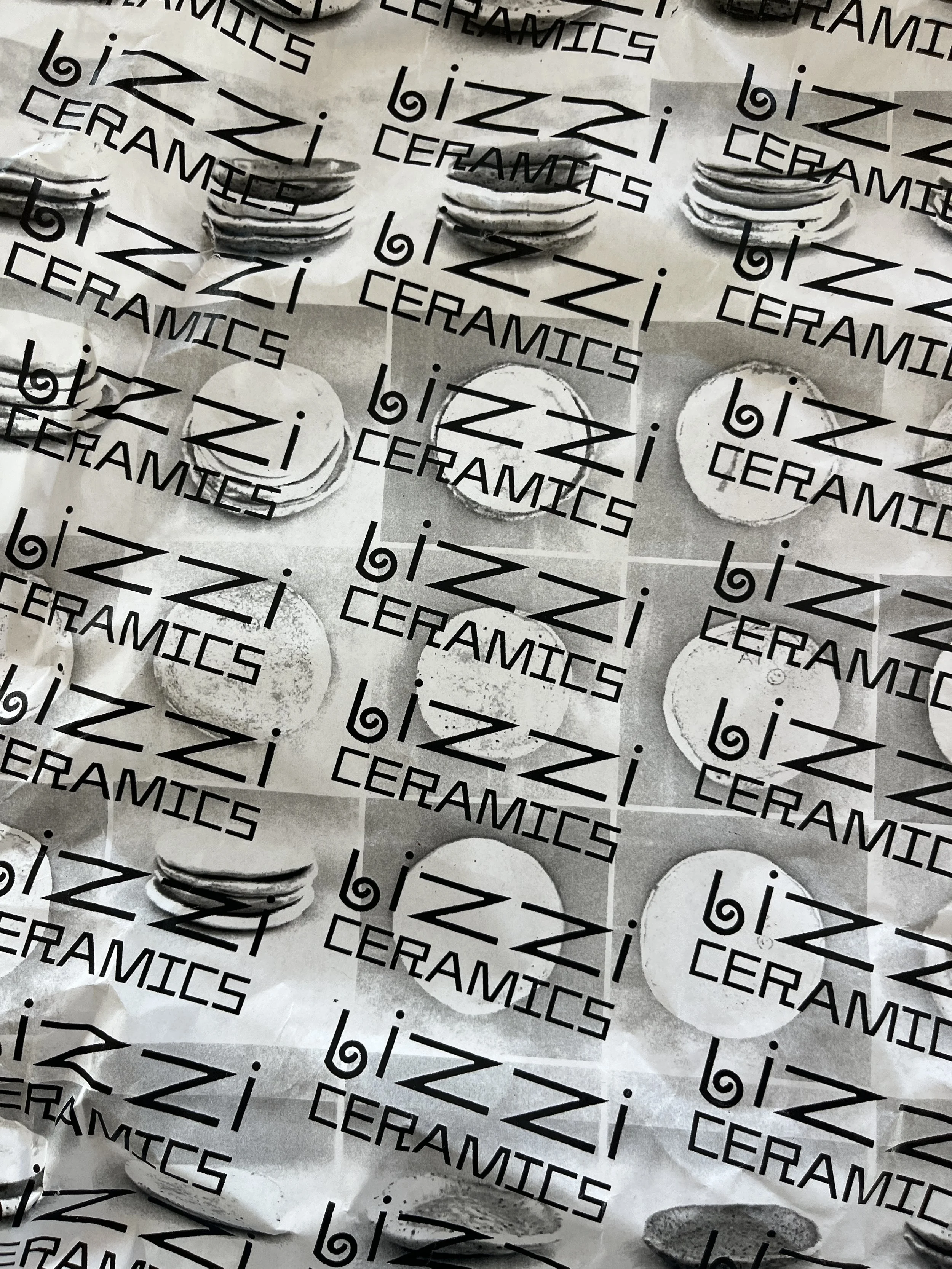 Crumpled black and white packaging paper with the logo and text "bzi CERAMICS" printed repeatedly.