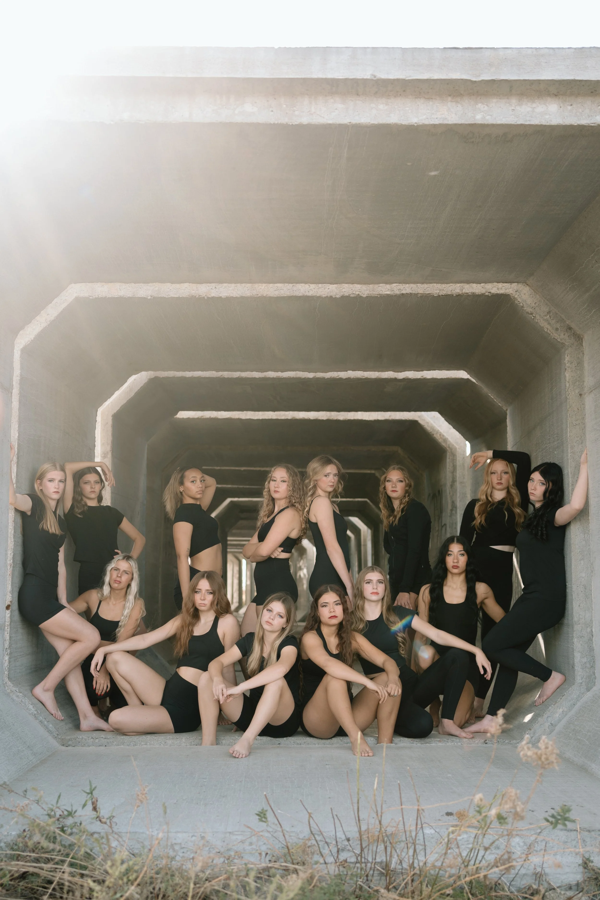 Competitive dancers pose in a group wearing black dance athleisure wear.