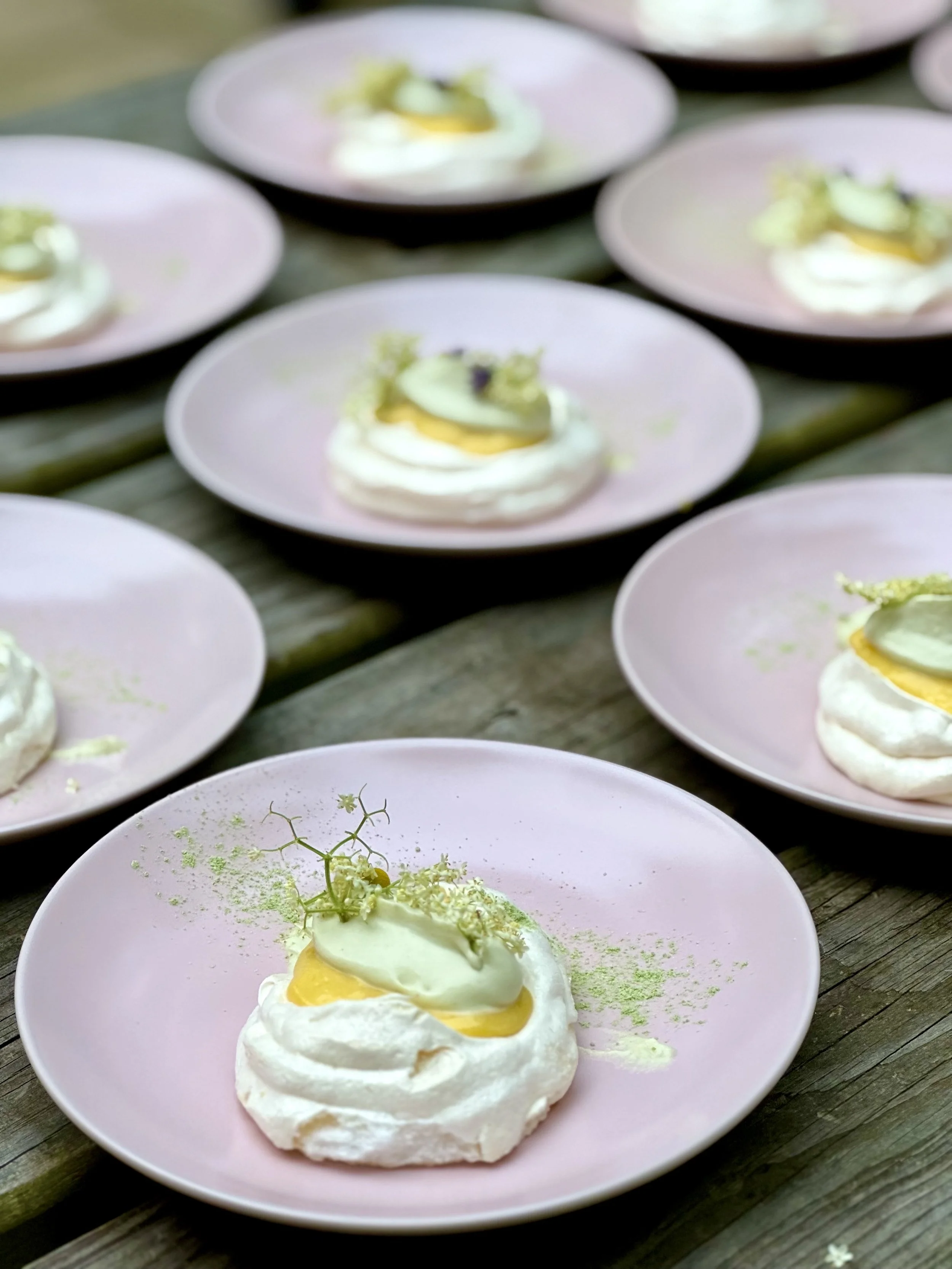 Several pink plates with a dessert topped with green and yellow garnishes, placed on a wooden surface.
