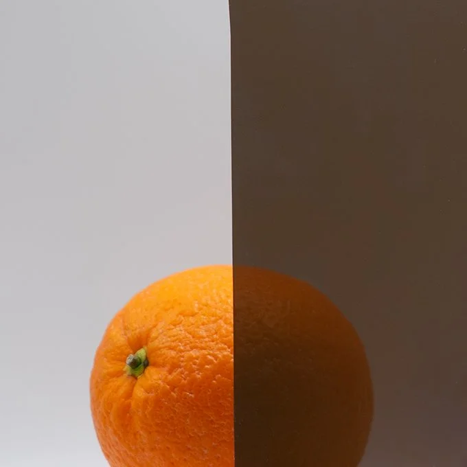 Half of the image shows a bright orange tangerine, and the other half shows a dark background with a dark-colored fruit, possibly an orange, in front of it.