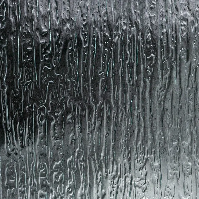 Rainwater streaming down a glass window, creating streaks and patterns.