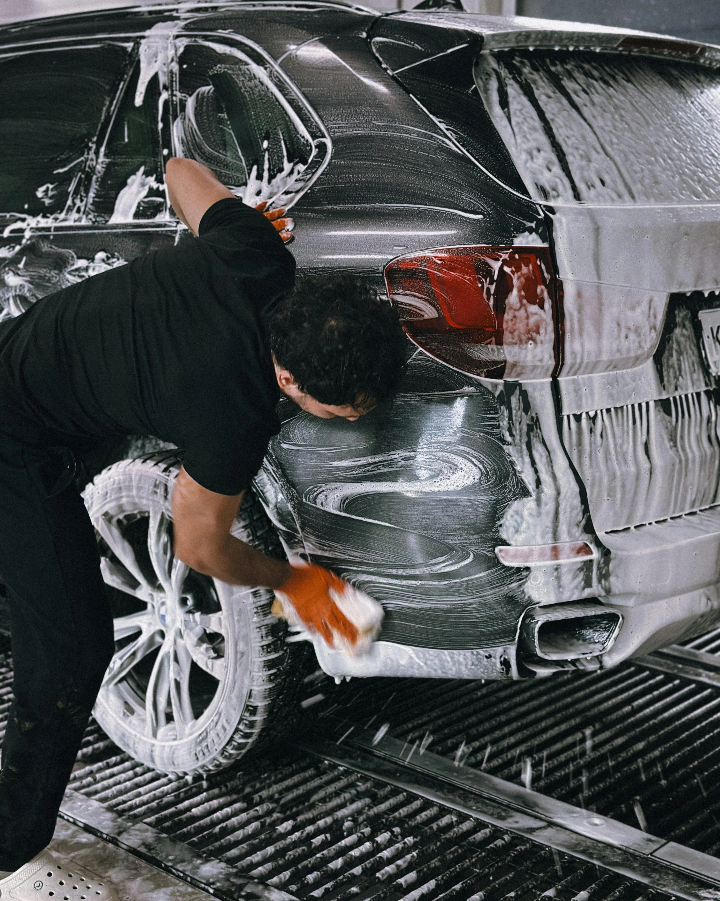 Person washing a black car with soap and sponge in a car wash station.