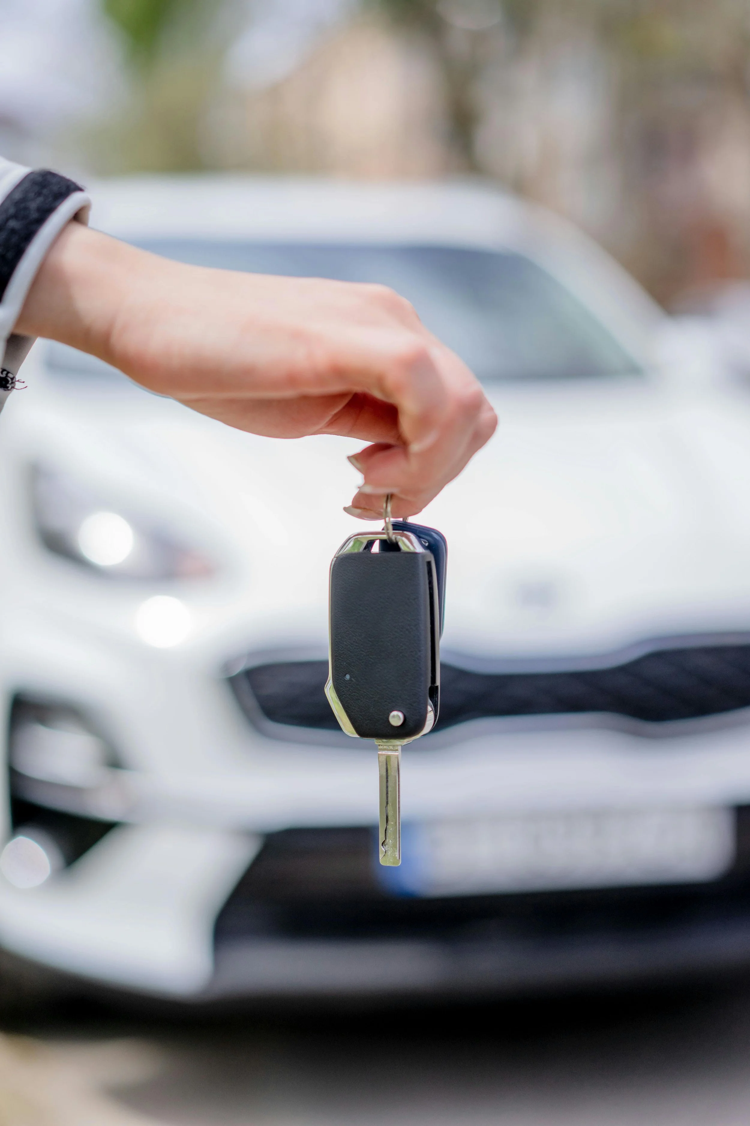 Close-up of a person holding car keys in front of a white car with a blurred background.