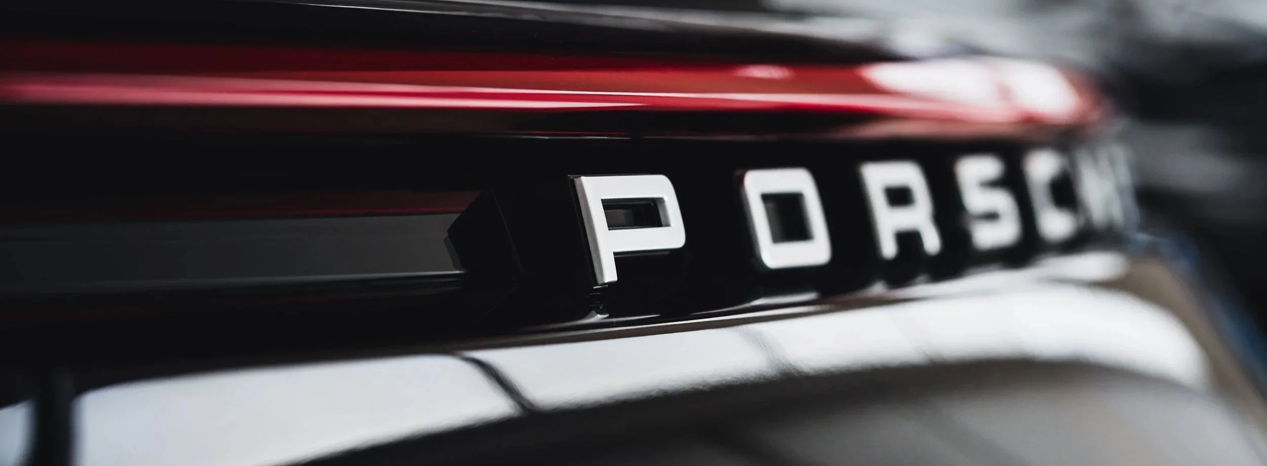 Close-up of a black car's rear badge displaying the word 'Porsche' in chrome letters.