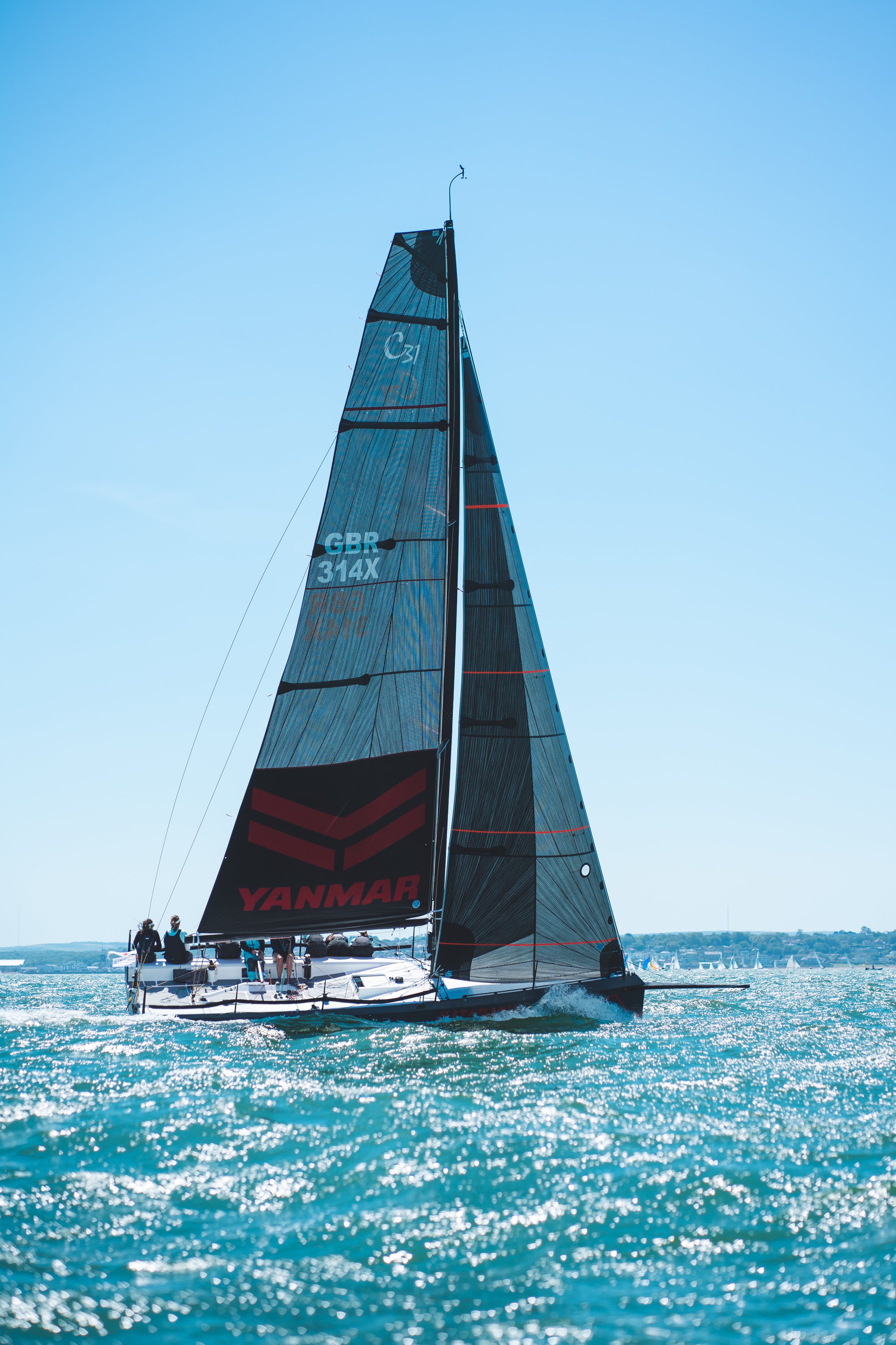 A sailboat with black and red sails on the water during the day.