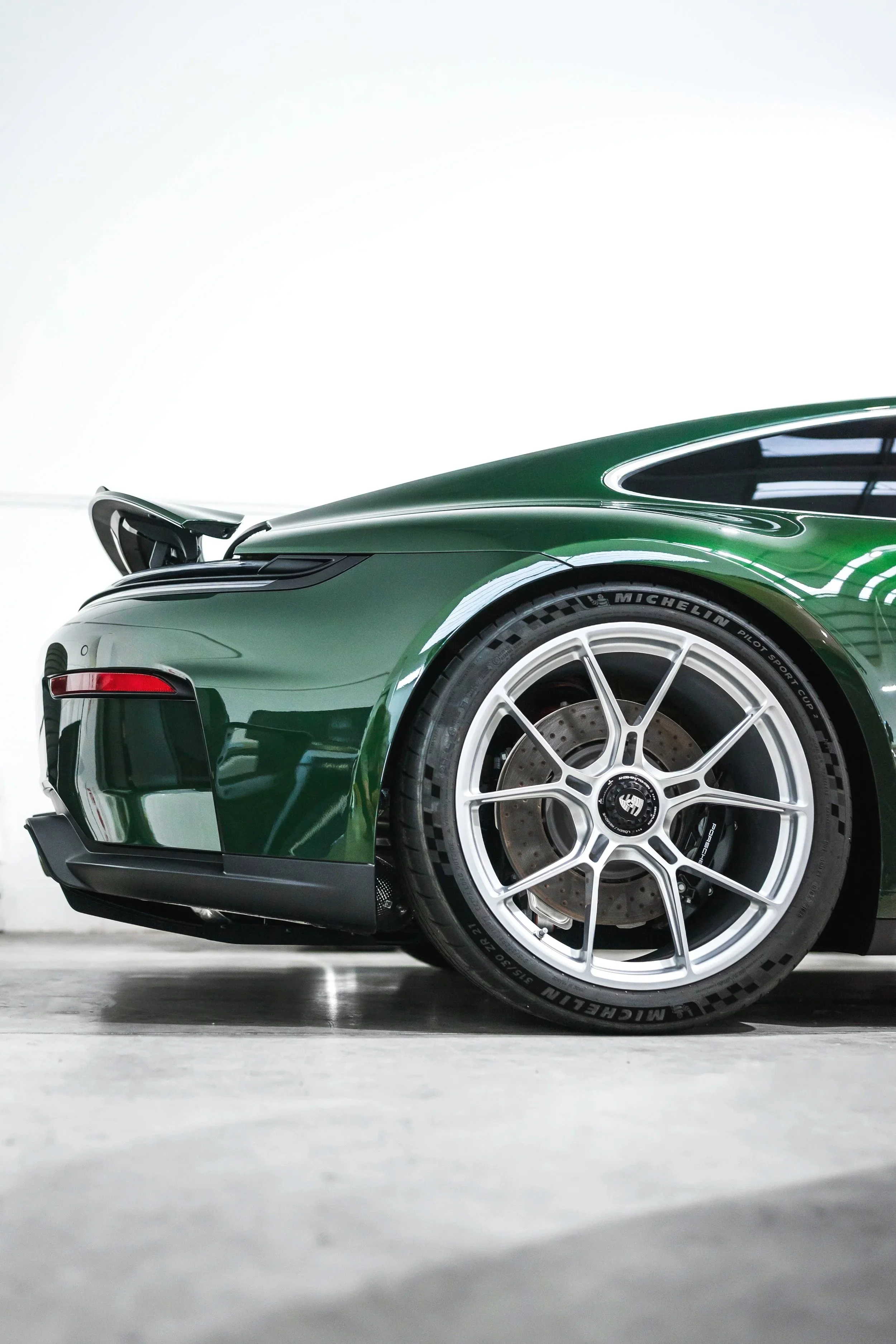 Close-up of the front part of a sleek green sports car with white alloy wheels and Michelin tires, parked indoors.