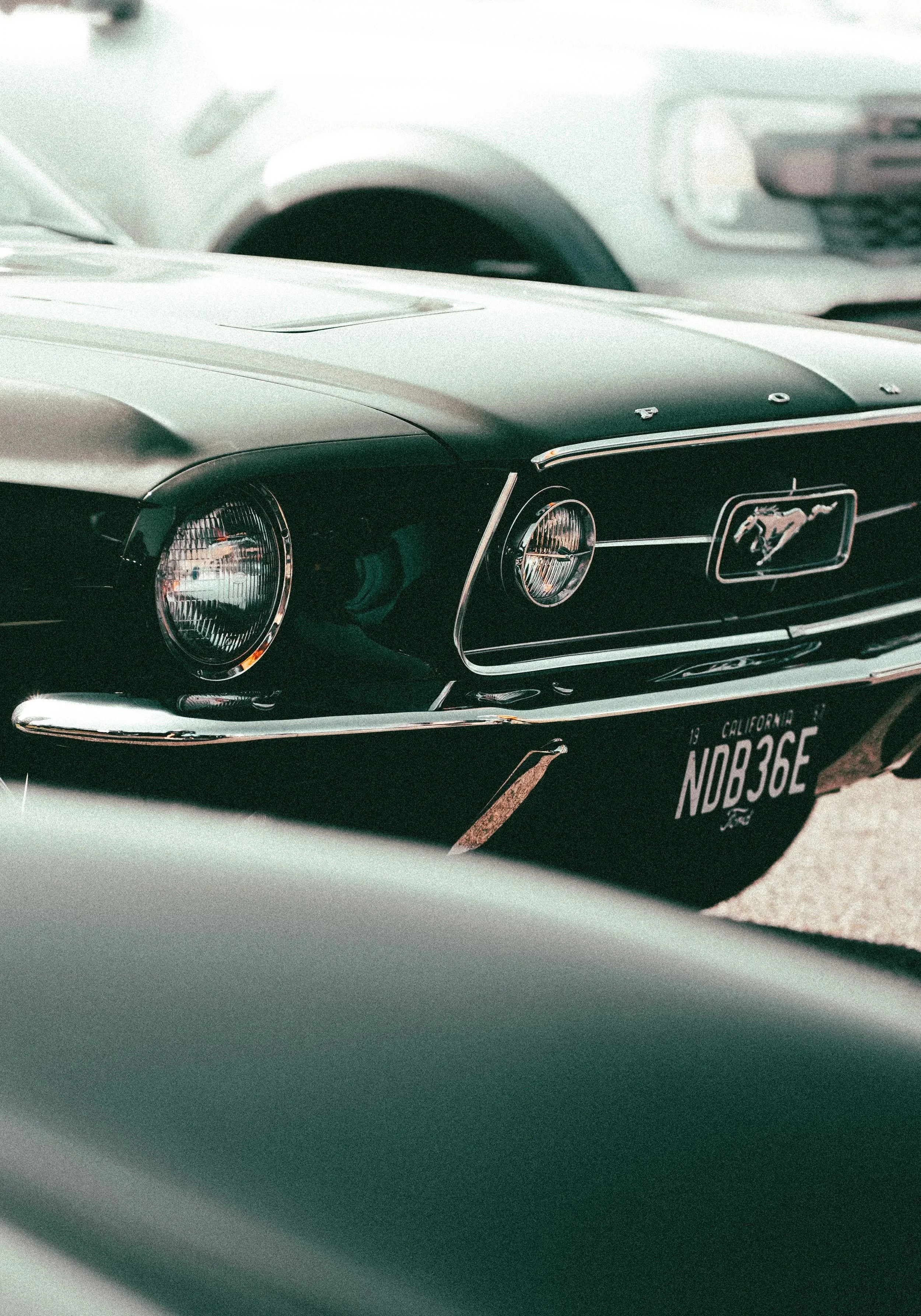 Close-up of a vintage black Ford Mustang car with a California license plate, parked alongside other cars in a parking lot.