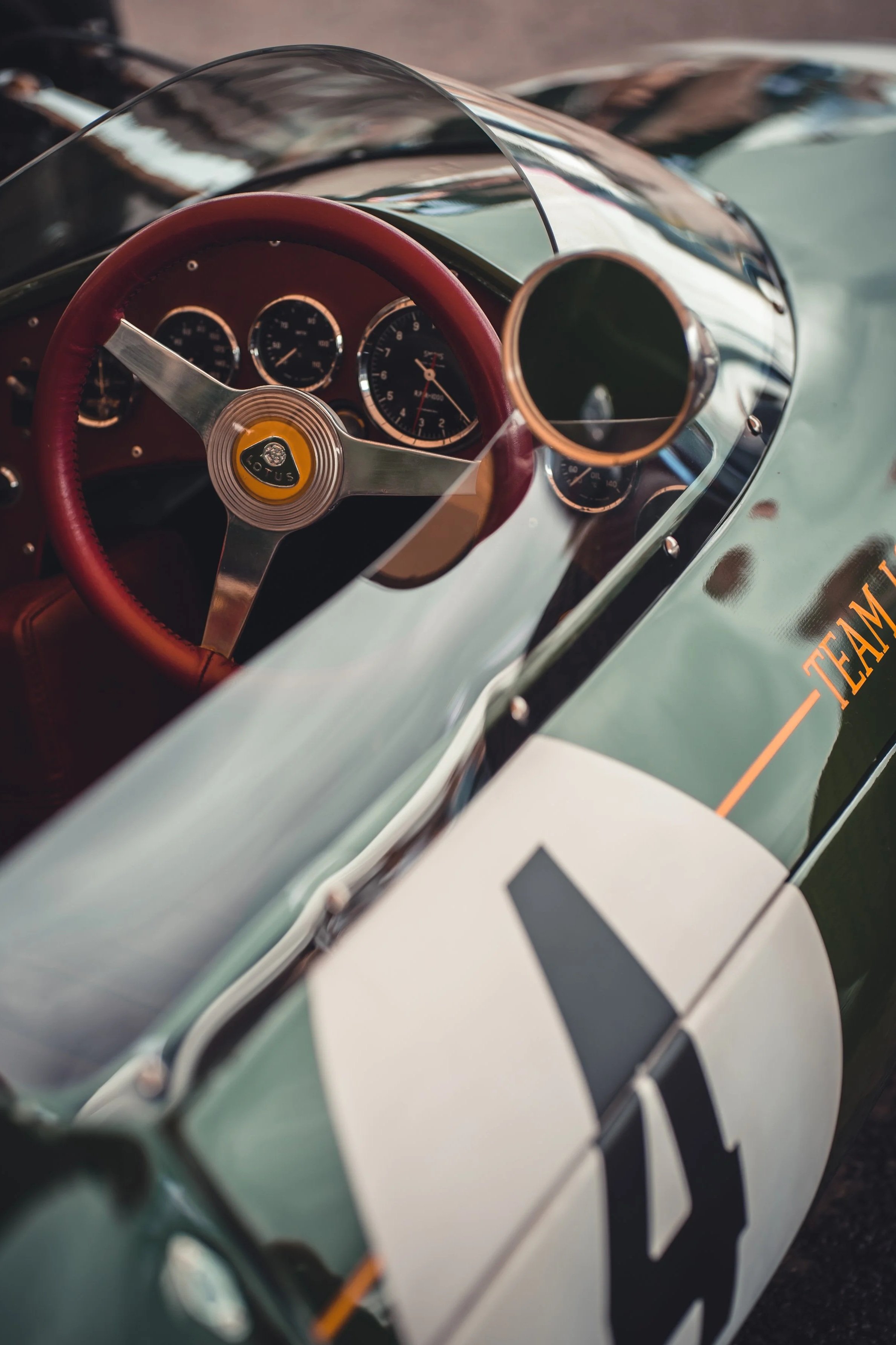 Close-up of a vintage race car's interior, showing the steering wheel, dashboard gauges, and a side mirror with a racing number '4' on the body.