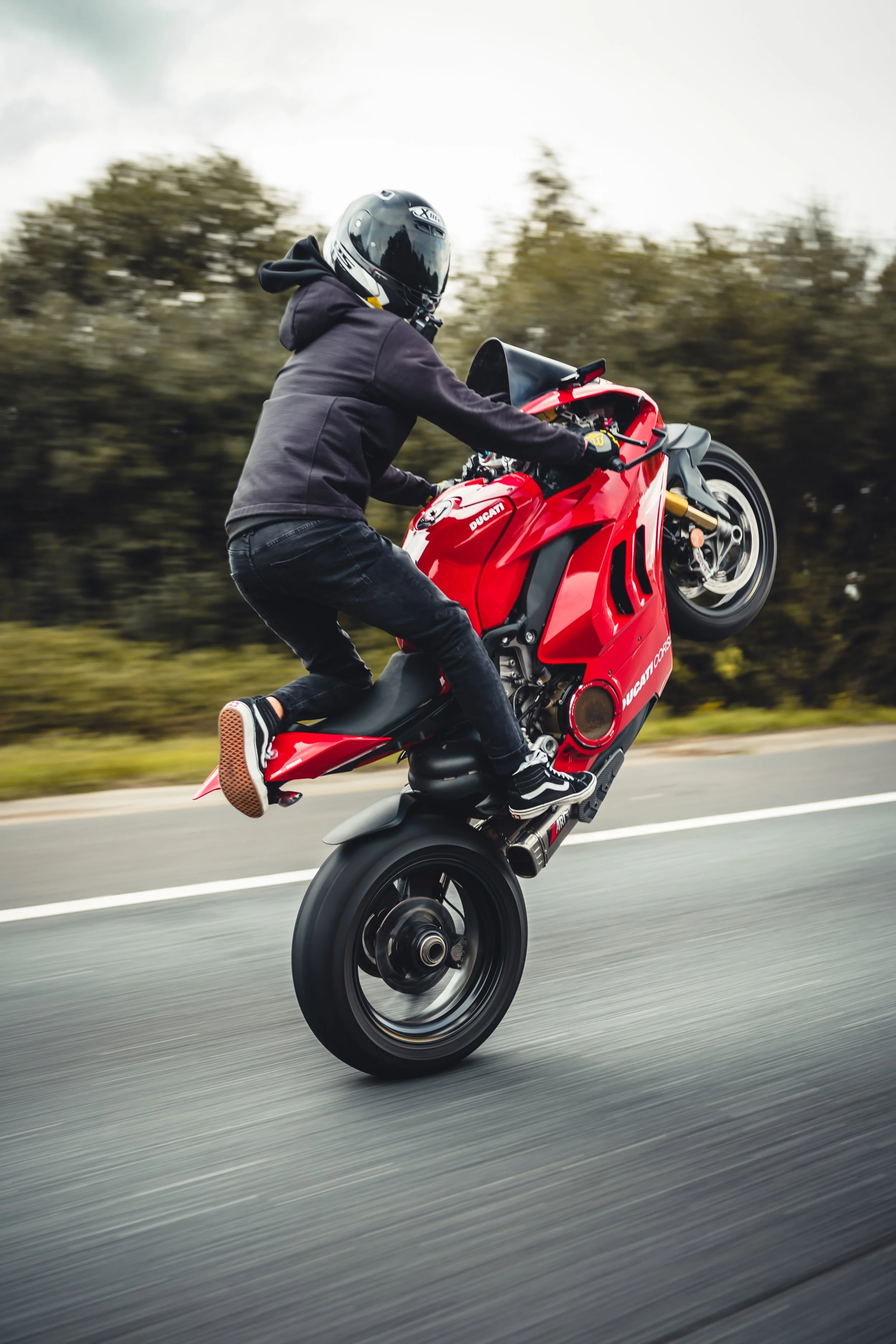 A person performing a wheelie on a red Ducati motorcycle on a road