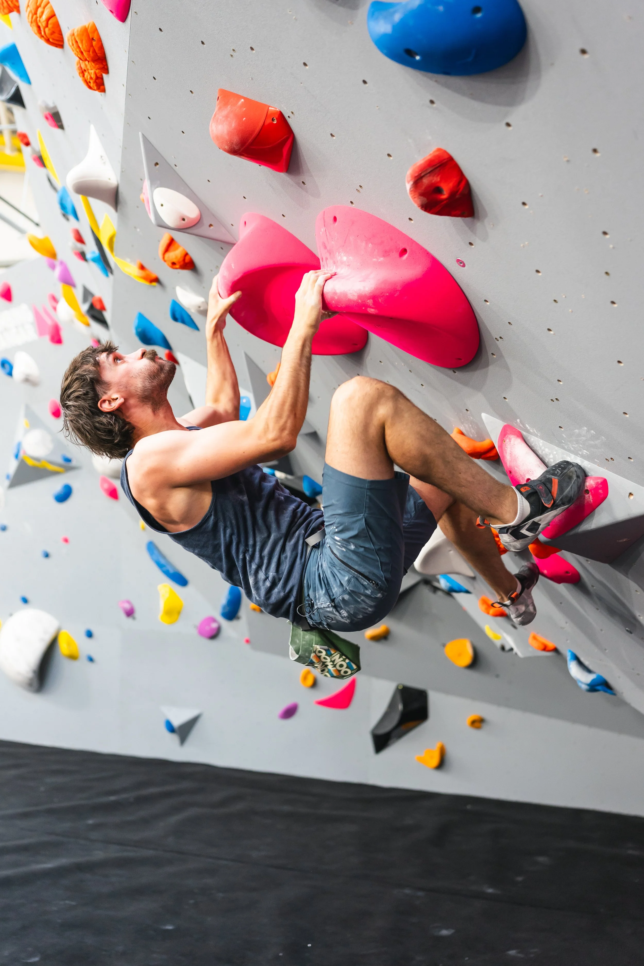Man bouldering on an indoor climbing wall with colorful holds.