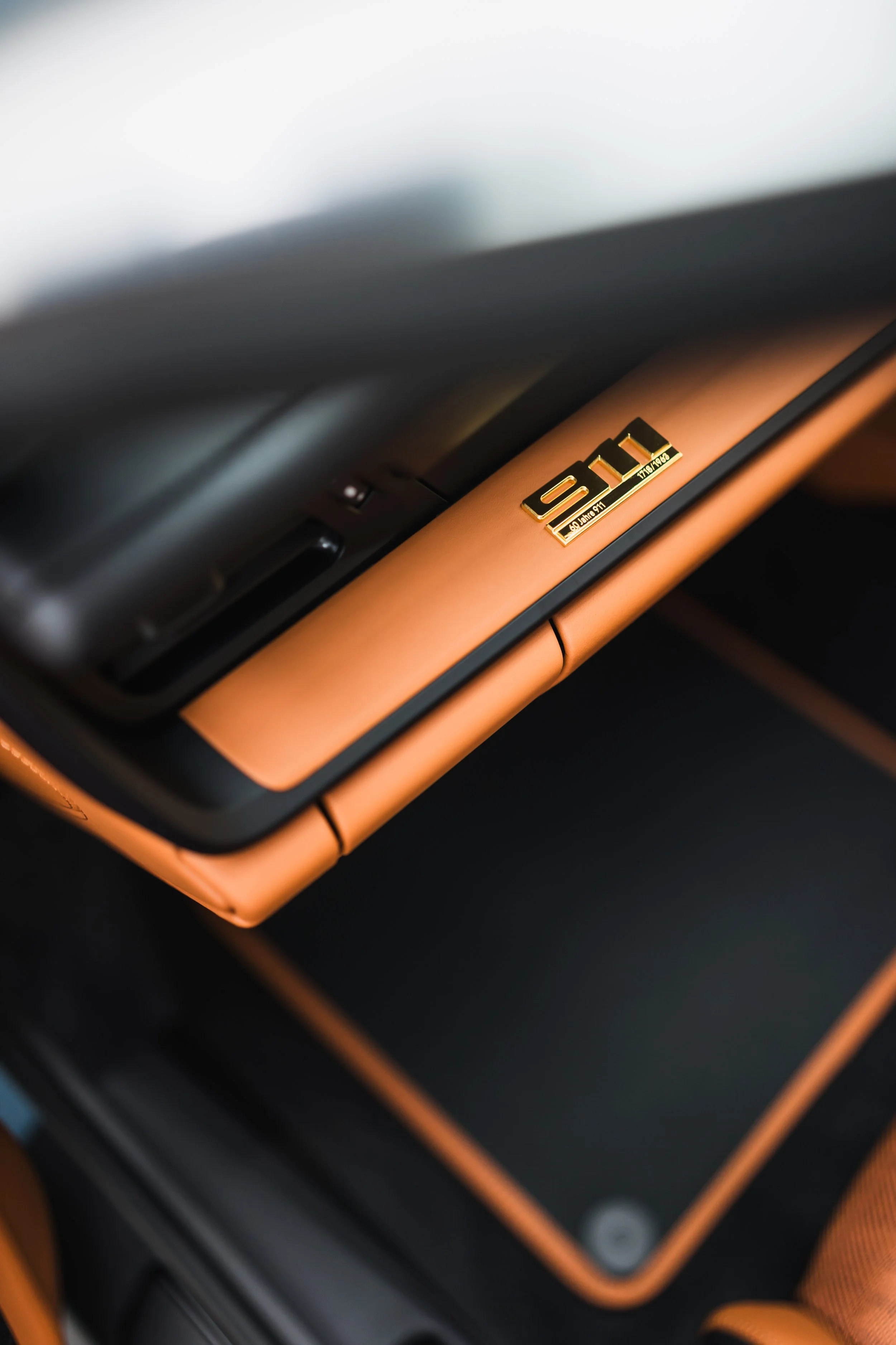 Close-up of a luxury car interior with a gold badge that reads 'V12' on a tan leather trim.