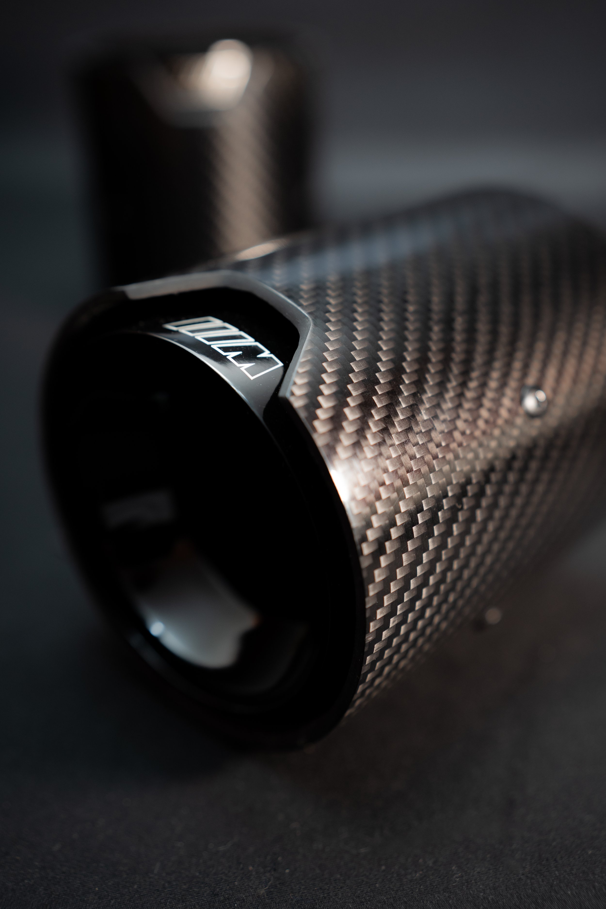 Close-up of a carbon fiber exterior with a focus on a cylindrical object with a sleek, textured surface and the brand name "NOEL" visible.