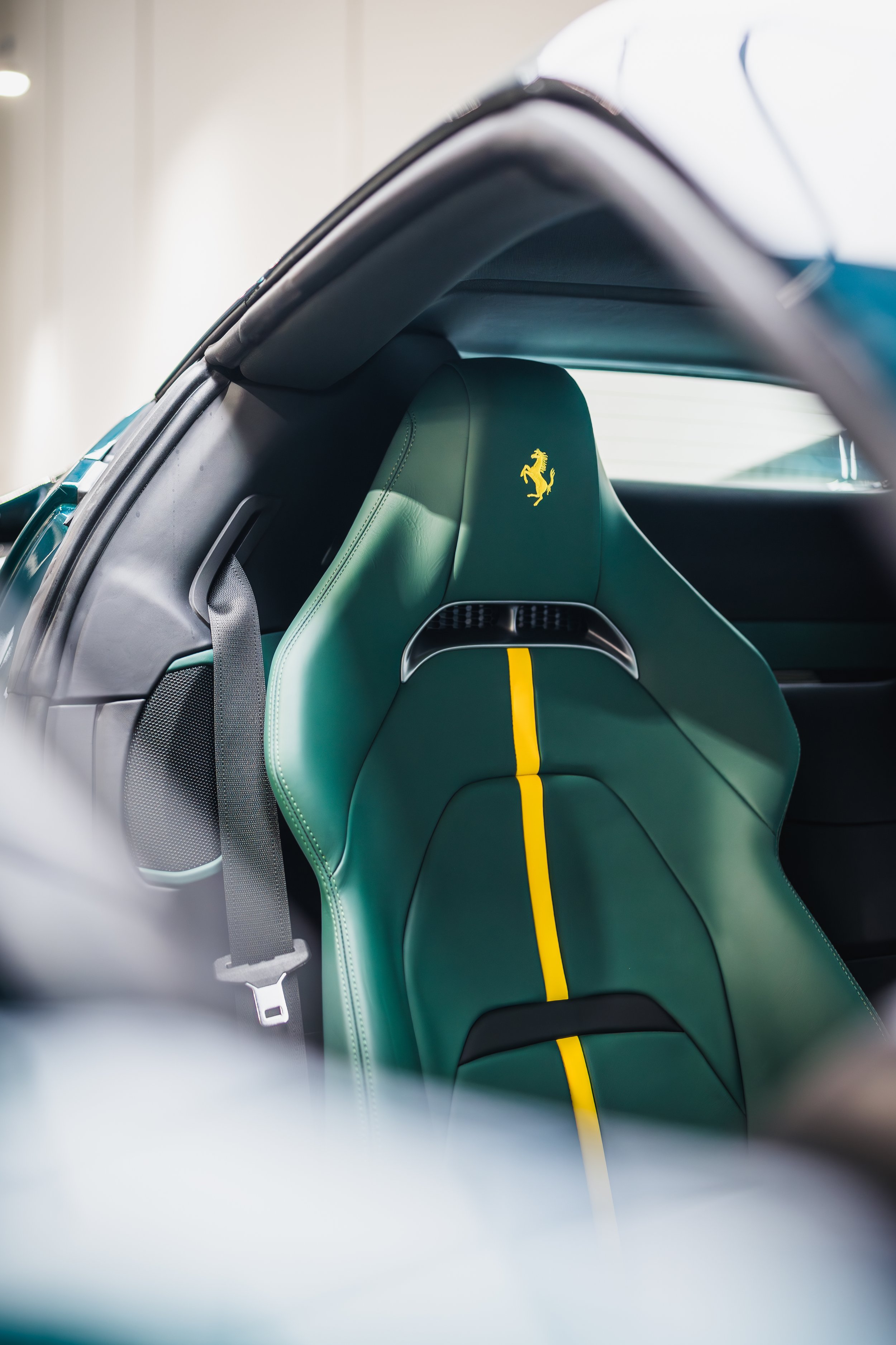 Close-up of the green leather seat in a Ferrari, featuring the yellow prancing horse logo on the headrest and a yellow stripe running down the center.