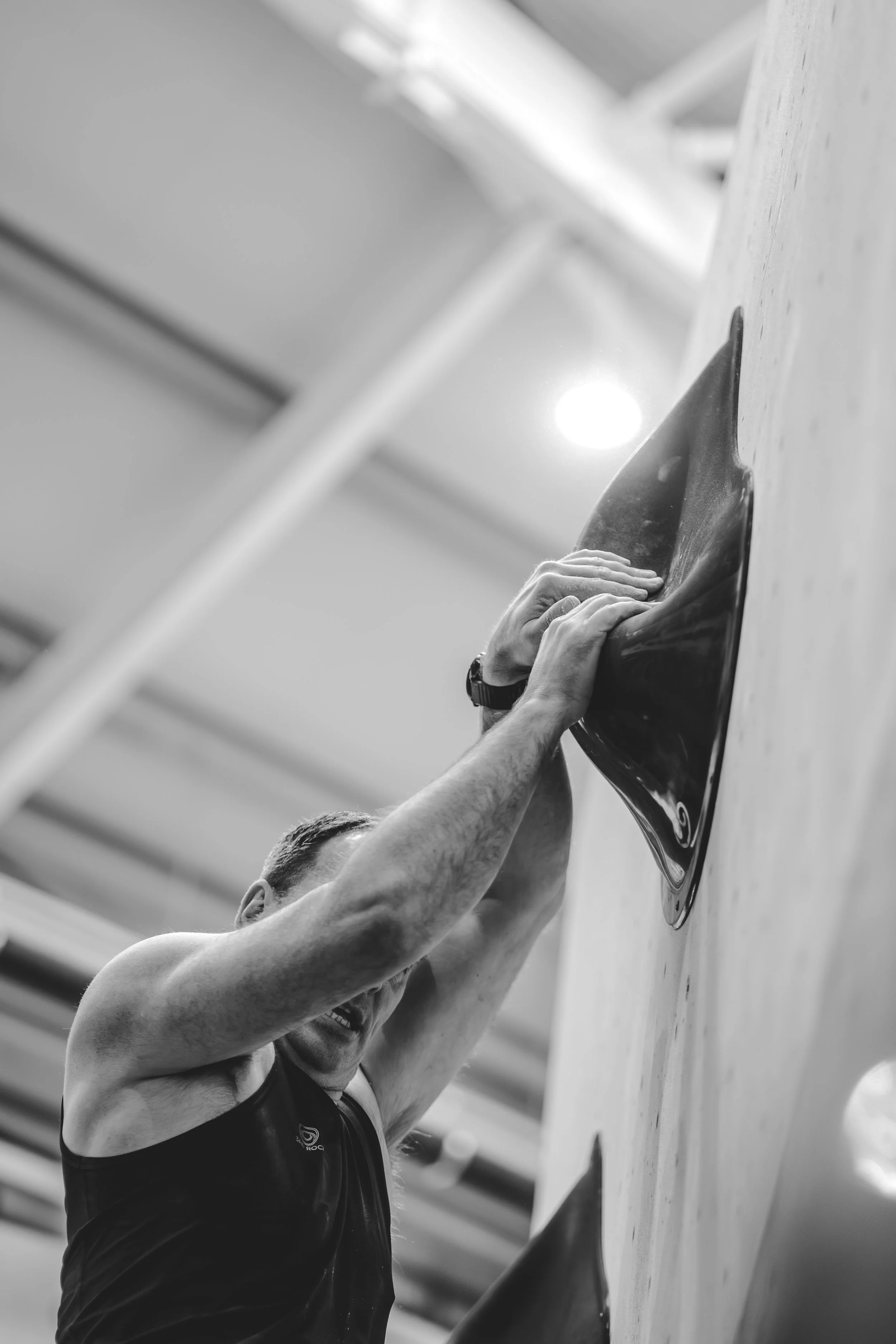A person rock climbing indoors, gripping a hold on a climbing wall.