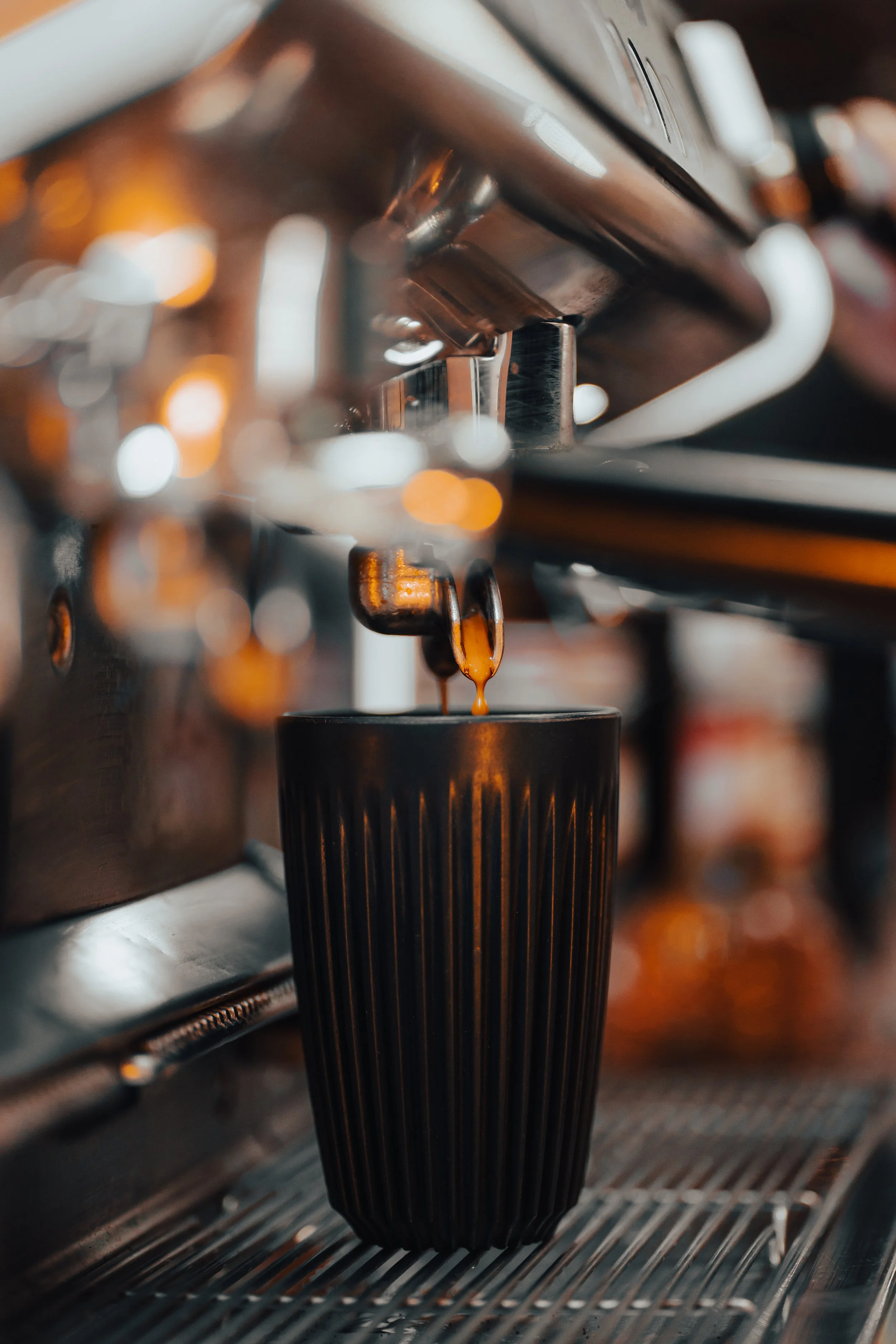 Close-up of coffee espresso machine pouring dark coffee into a black textured cup.