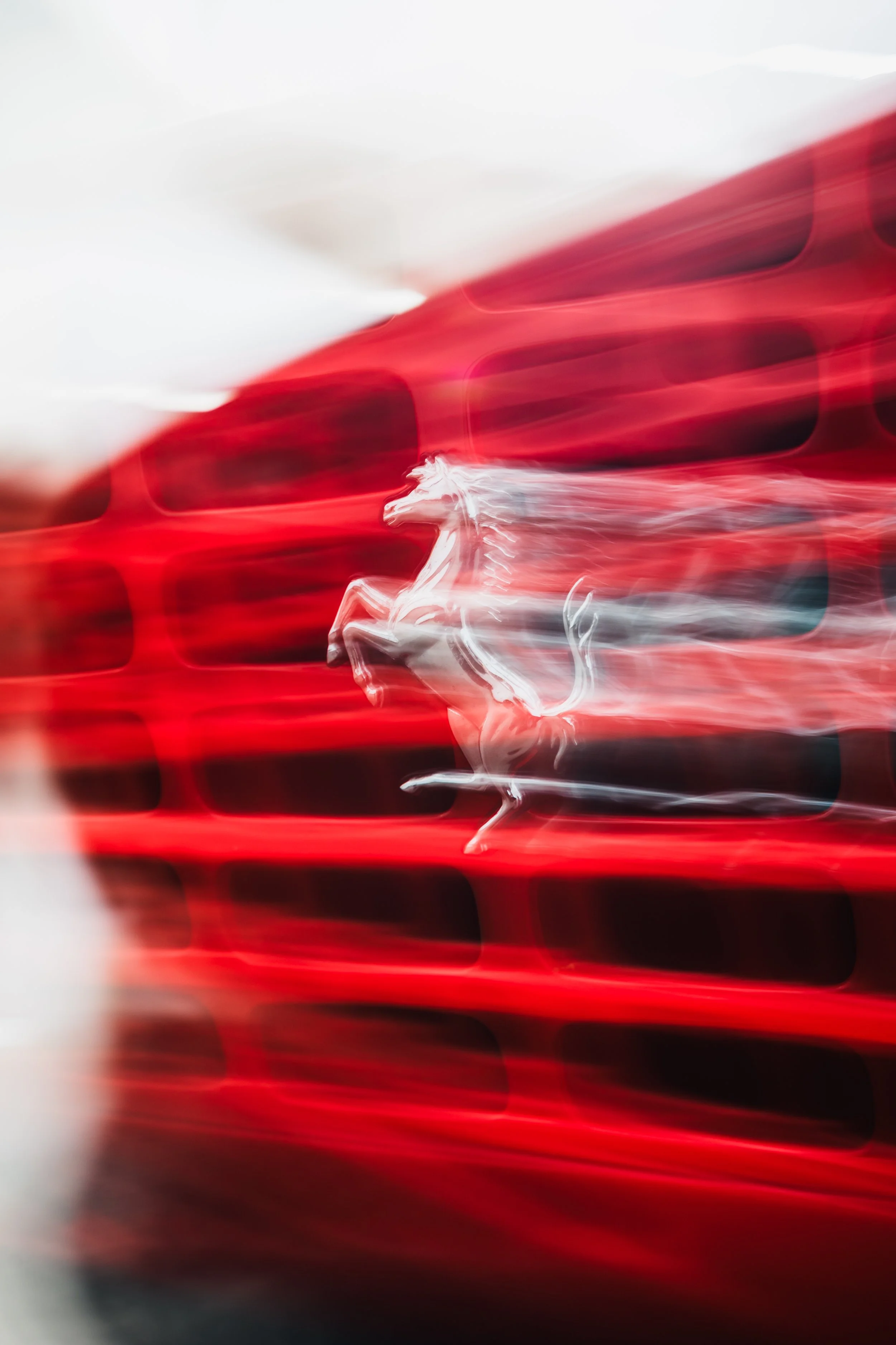 Blurred image of a Ferrari logo on a car grille with streaks of red and black.