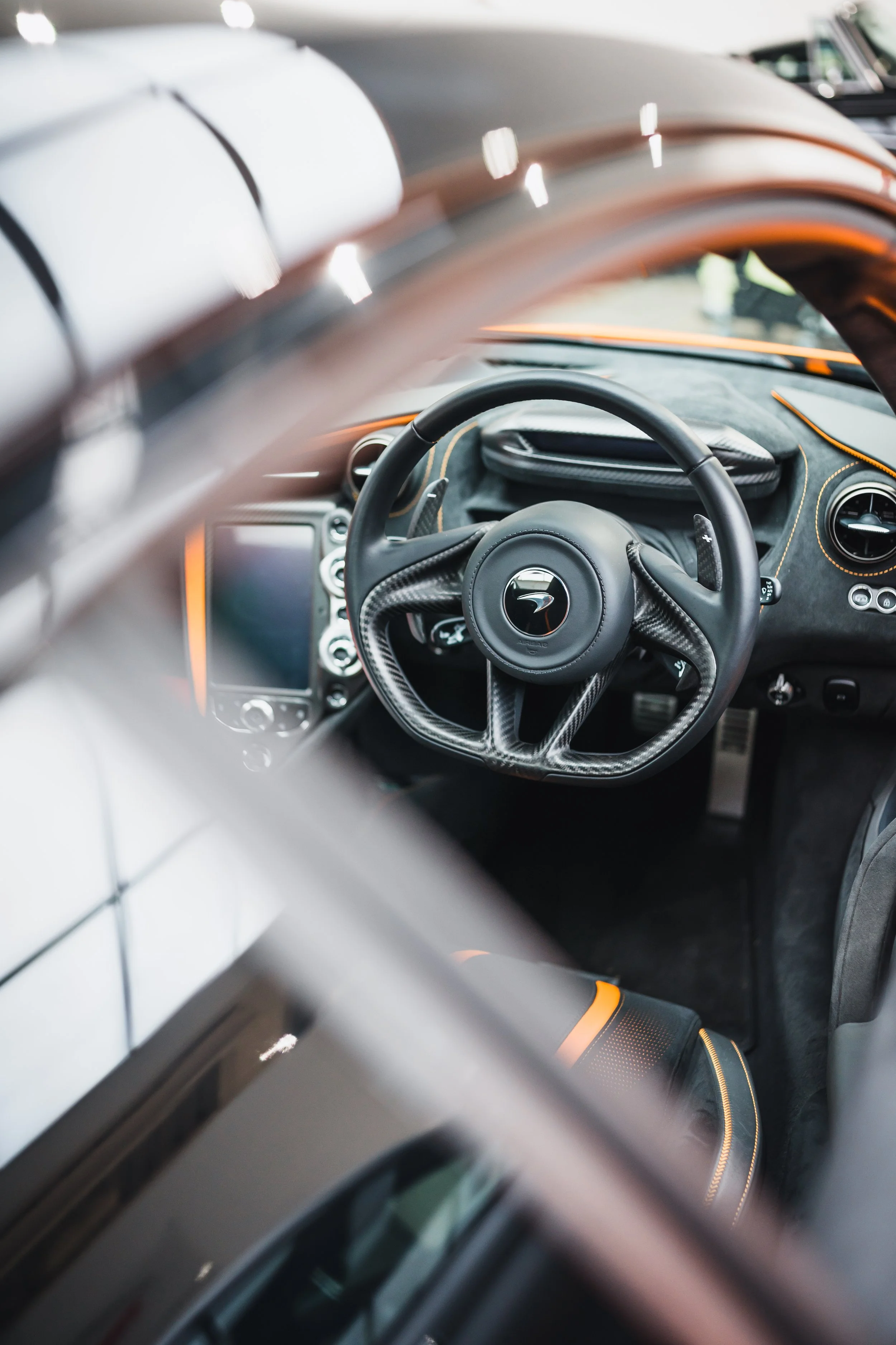Close-up view of a luxury car interior, showing a carbon fiber steering wheel and a digital display.