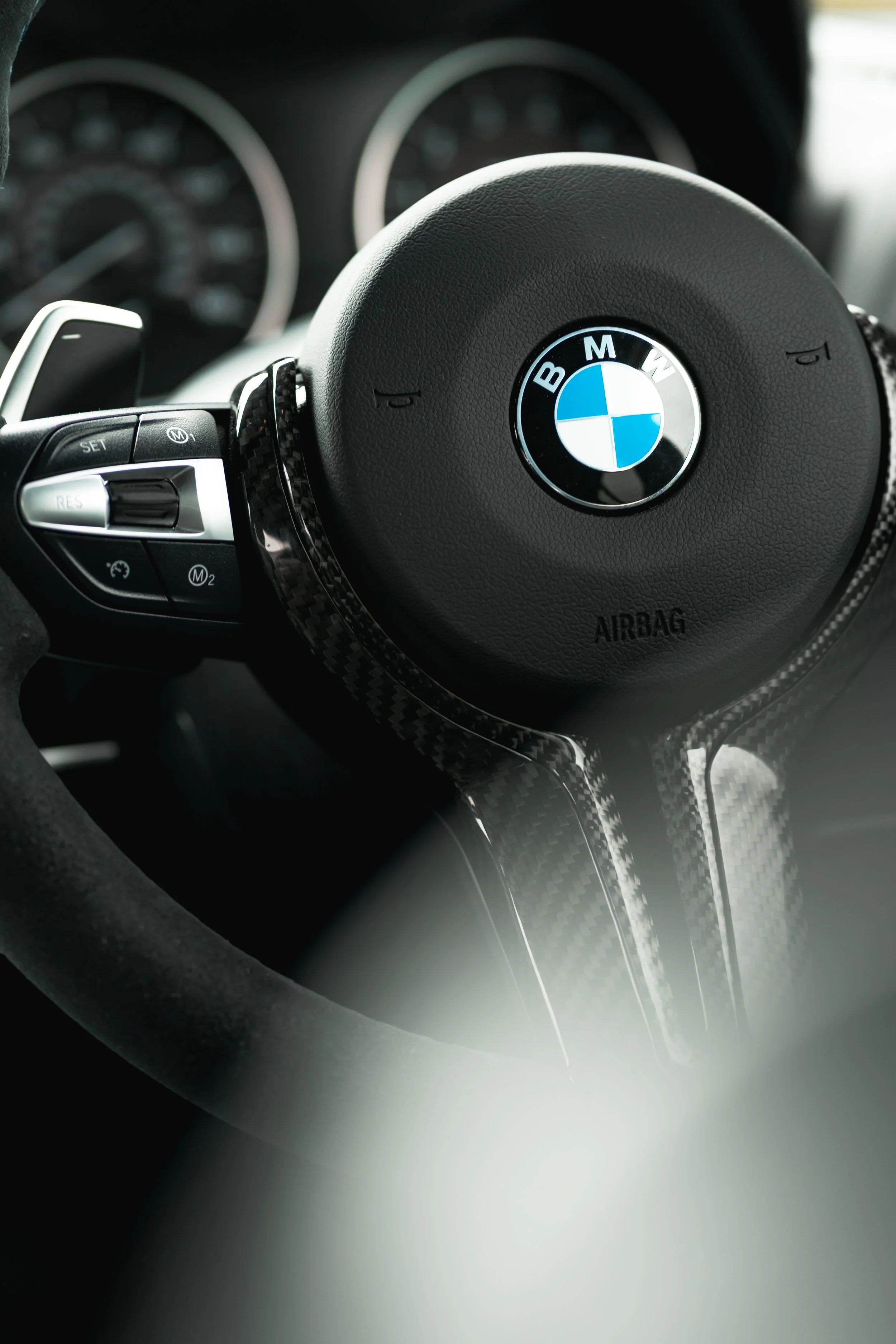 Close-up of a BMW car steering wheel with control buttons and a carbon fiber trim.