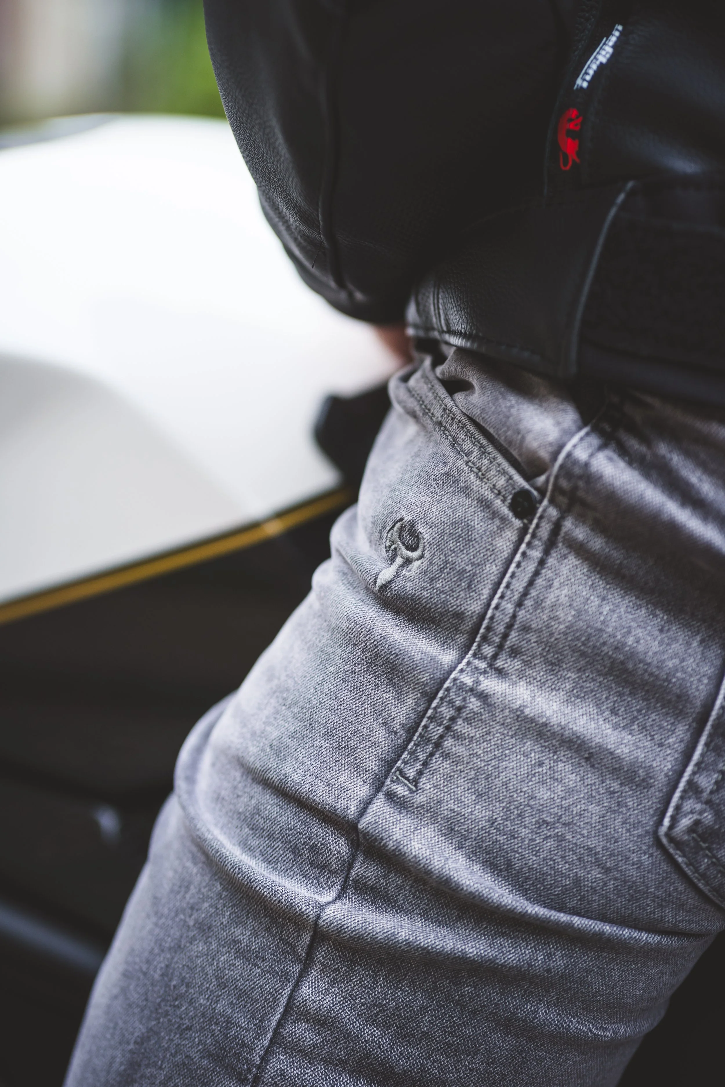 Close-up of a person in gray jeans and a black jacket, with part of a yellow and black object in the background.