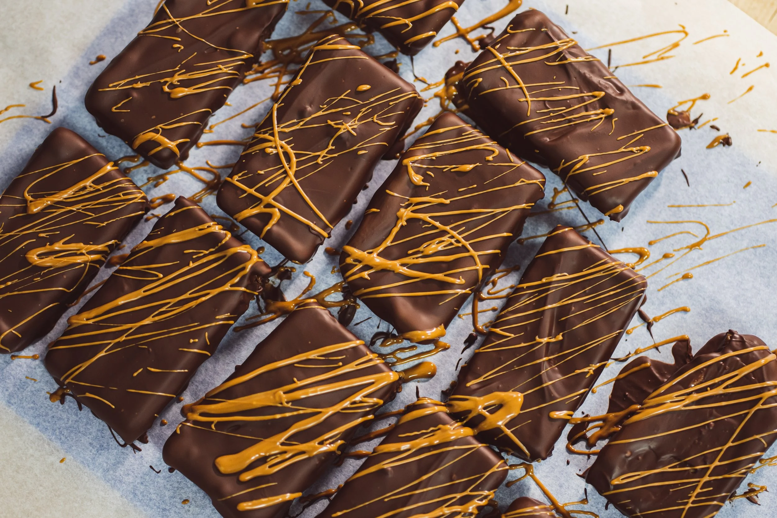Multiple chocolate-covered bars drizzled with caramel on a sheet of parchment paper.