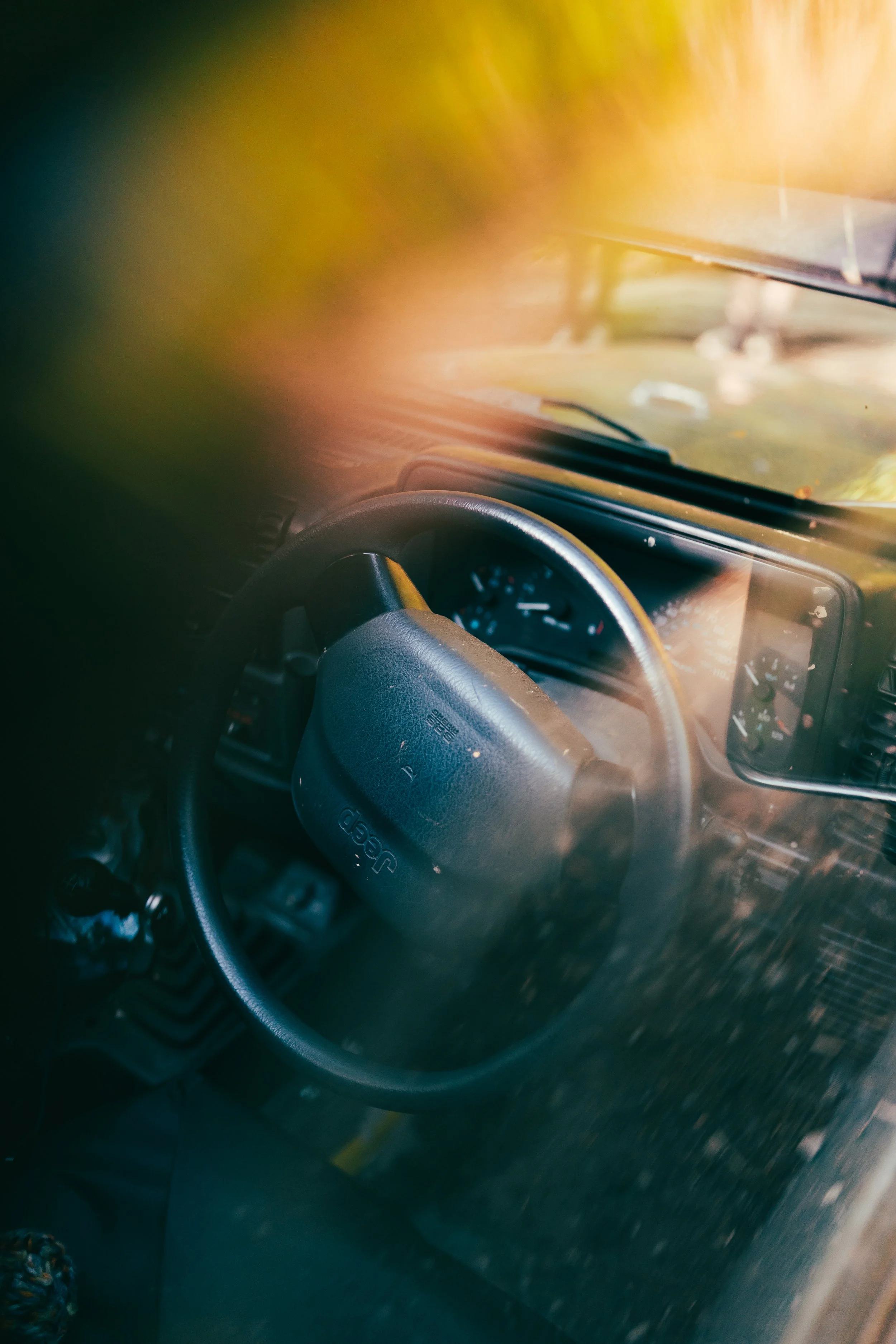 View of a car interior showing the steering wheel and dashboard, with sunlight coming through the windshield and a blurry outdoor scene.