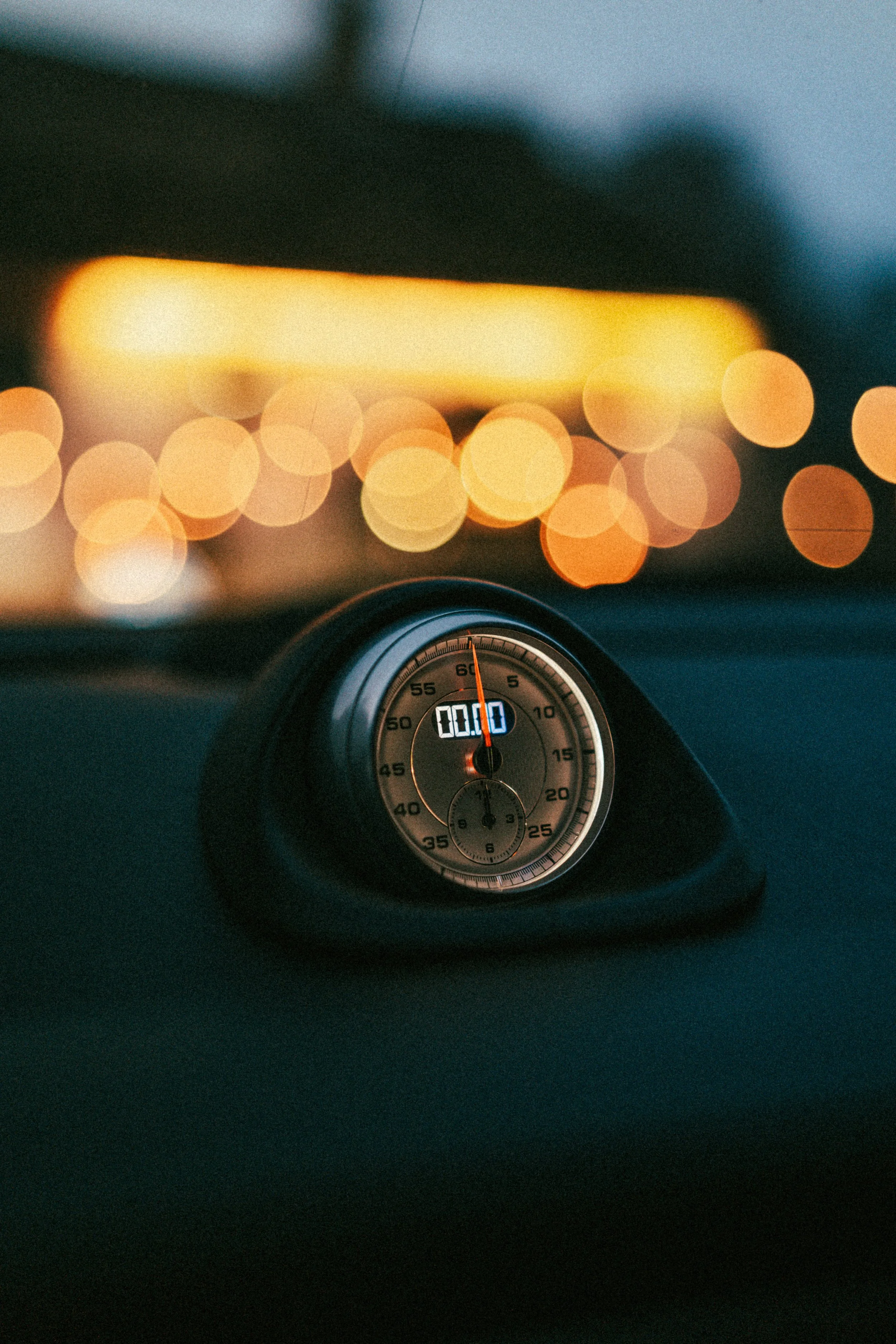 Close-up of a stopwatch on a car dashboard with blurred city lights in the background.