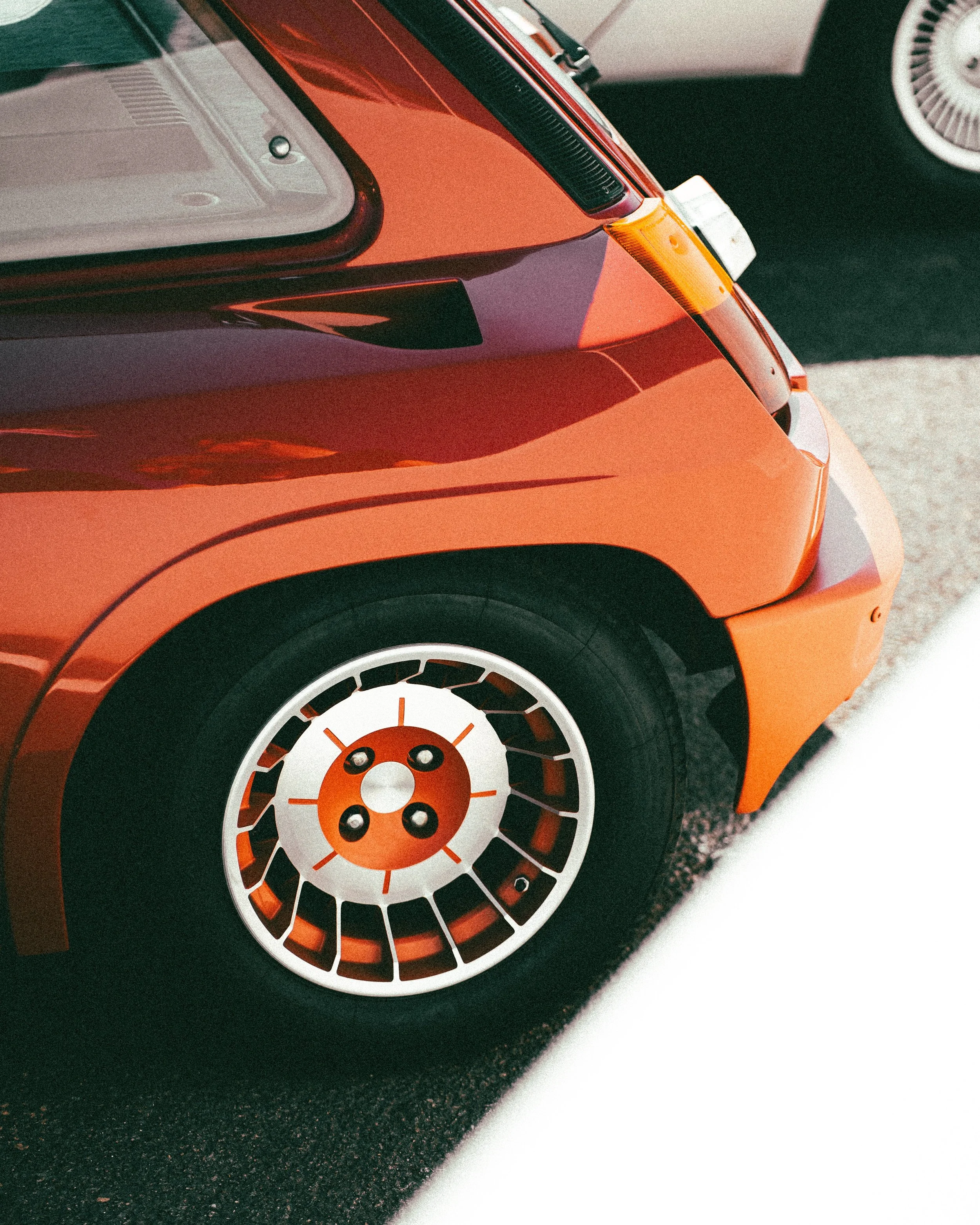 Close-up of a vintage orange sports car with distinctive wheel design parked on asphalt with a white line.