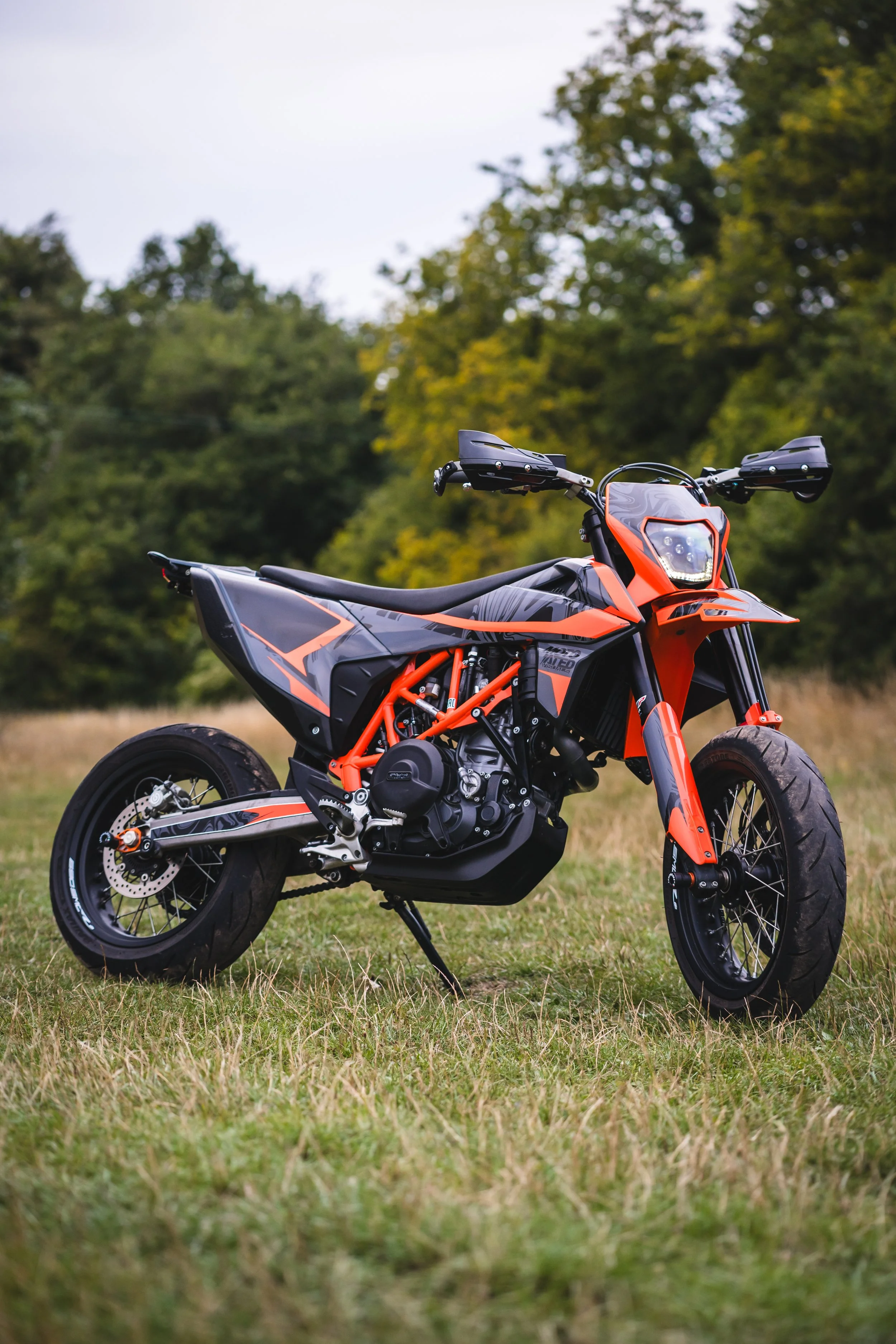 A KTM dirt bike motorcycle parked on grass with trees in the background.