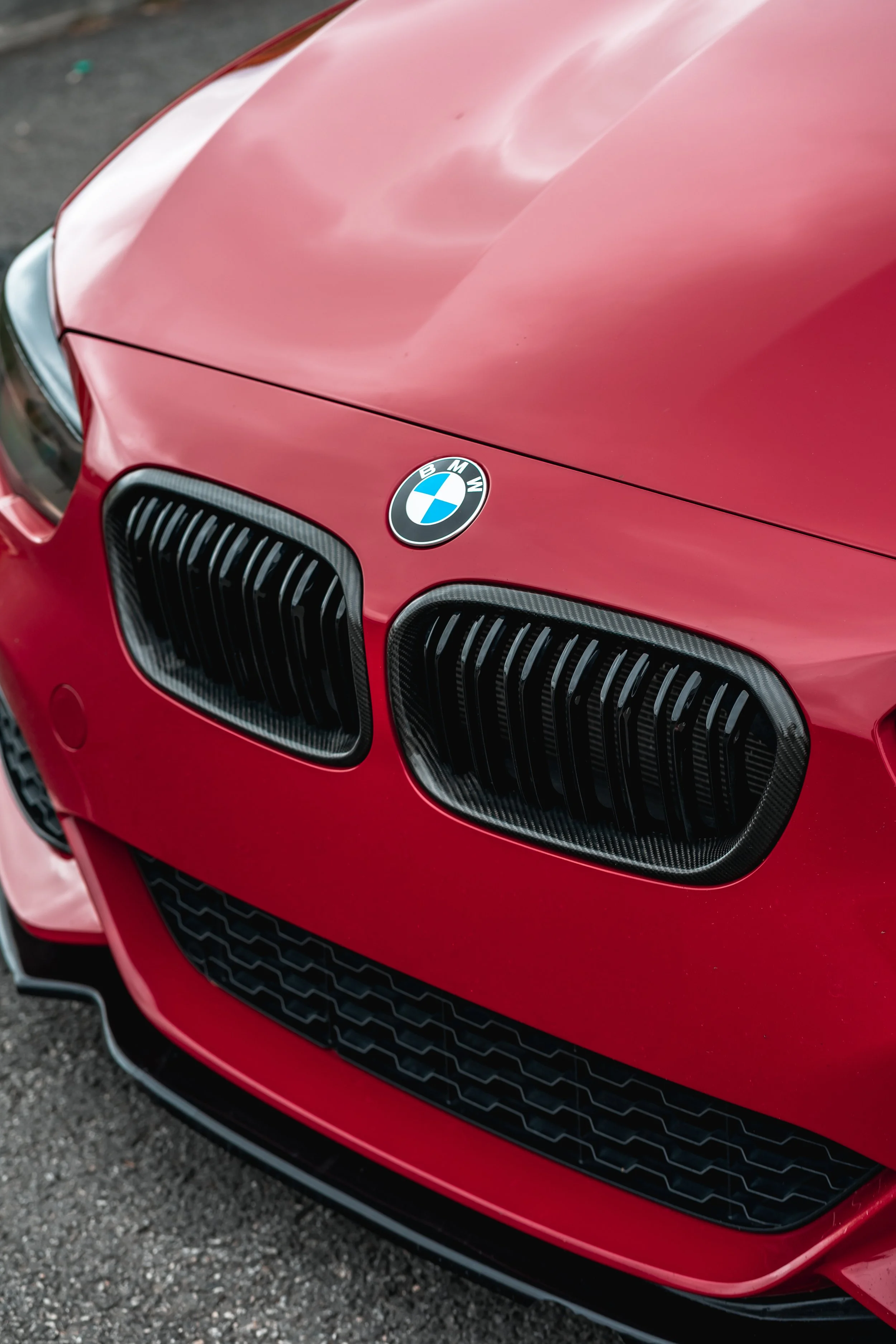 Close-up of the front of a red BMW car, showing the BMW logo, black kidney grille, and part of the front lower grille.