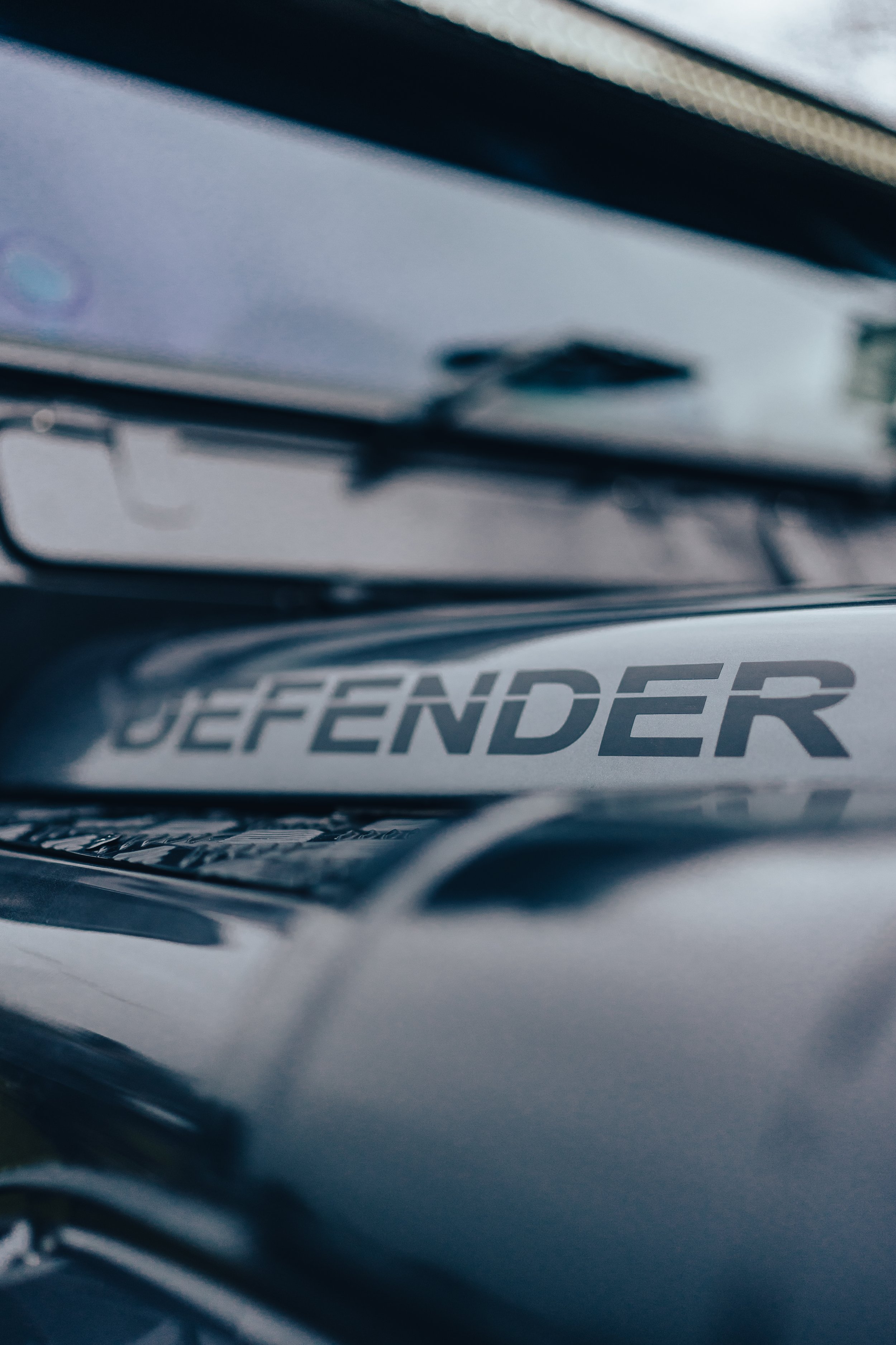 Close-up of a vehicle badge that reads 'DEFENDER' on the front of a black Land Rover Defender vehicle.